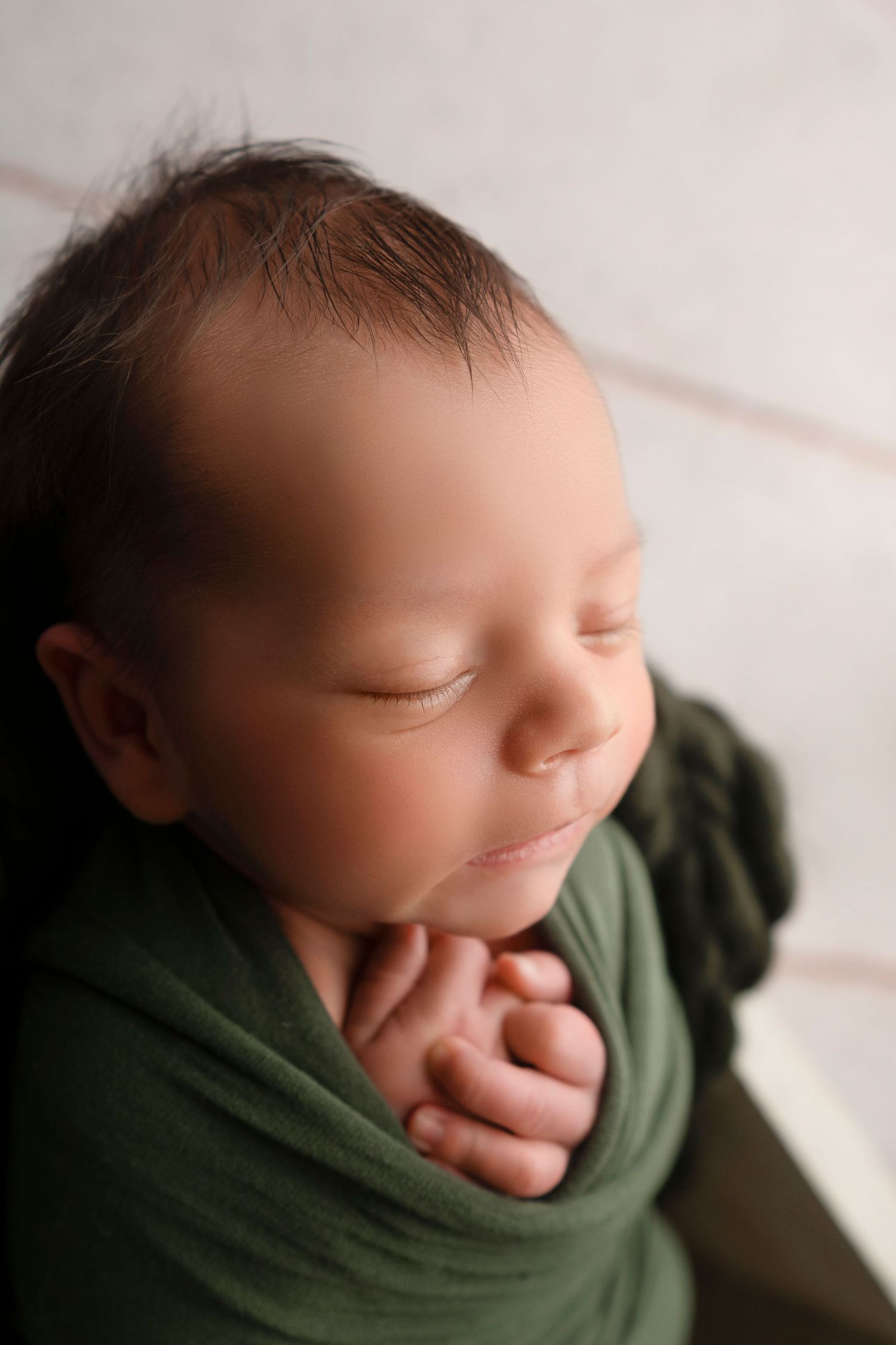 A sleeping newborn baby wrapped in a green swaddle blanket rests peacefully against a white background.