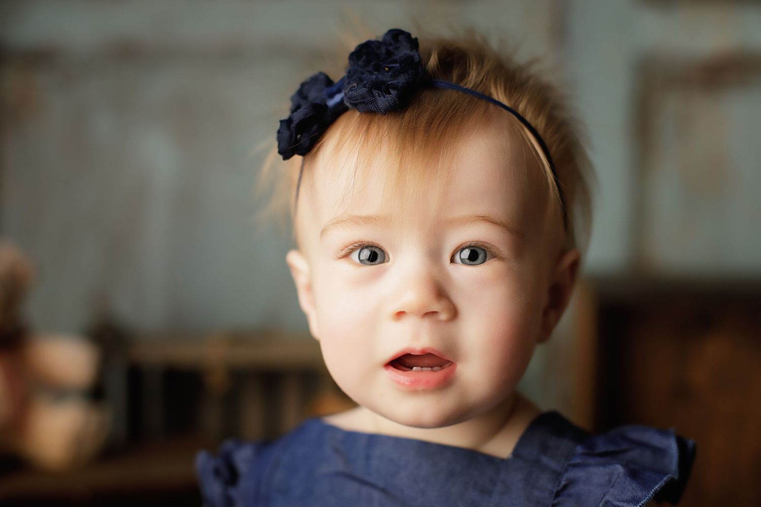 Small child wearing a navy blue dress and matching bow headband in a softly lit indoor setting.