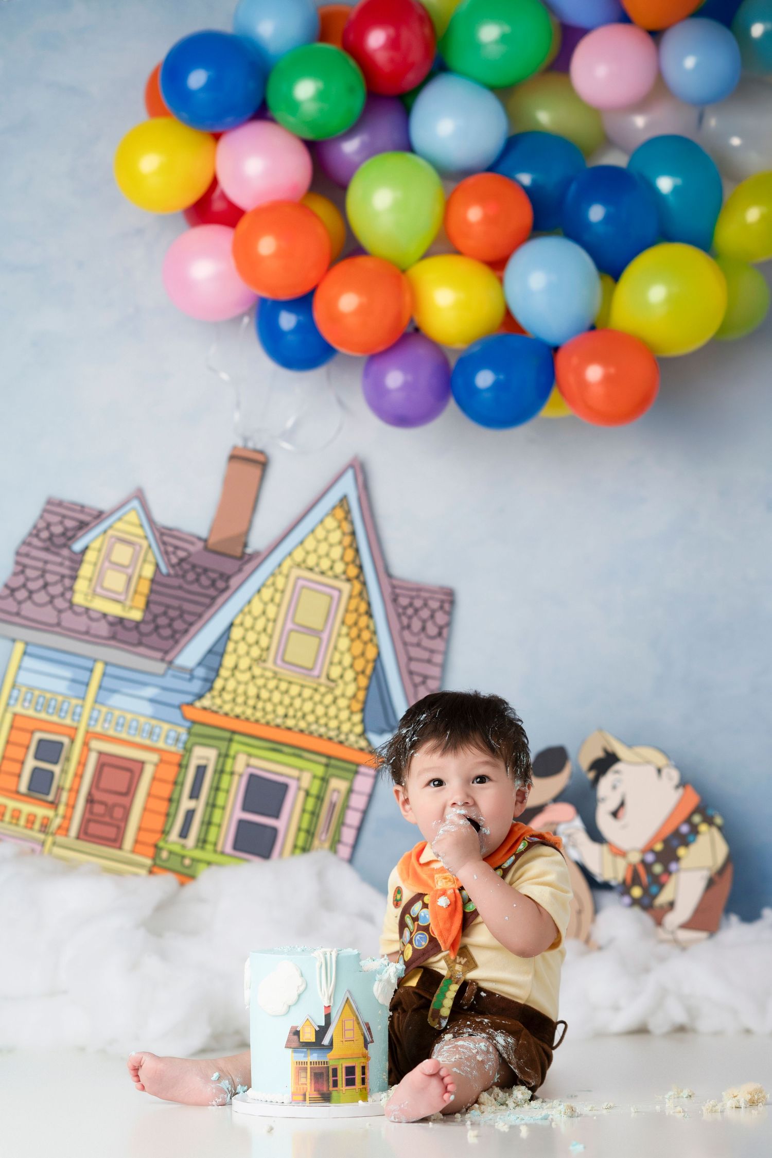 Colorful balloon arch with whimsical cartoon houses and fluffy white cotton clouds create a dreamy backdrop setup.