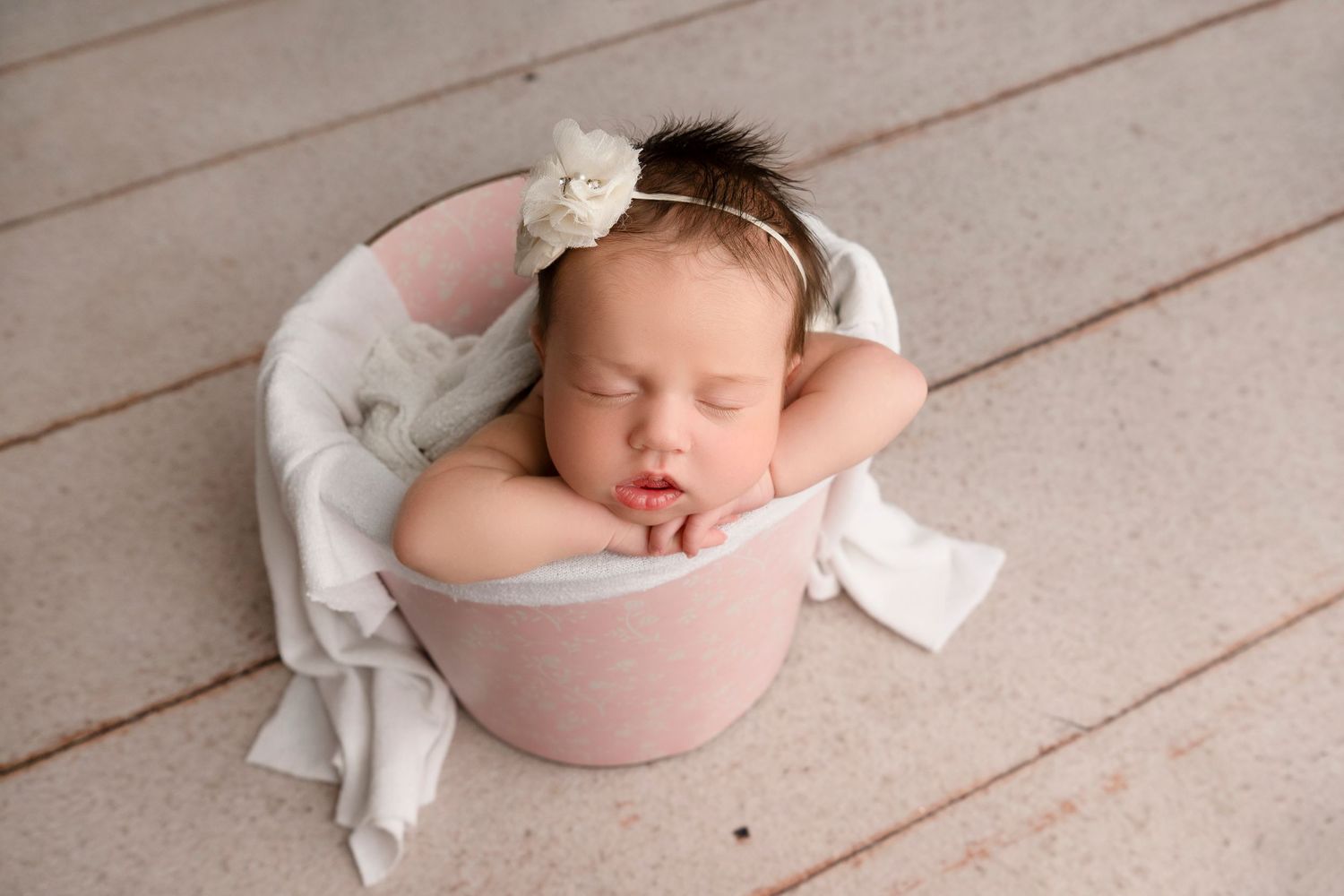 Series of newborn portraits showing baby sleeping in pink wrap and white bowl on rustic floor.