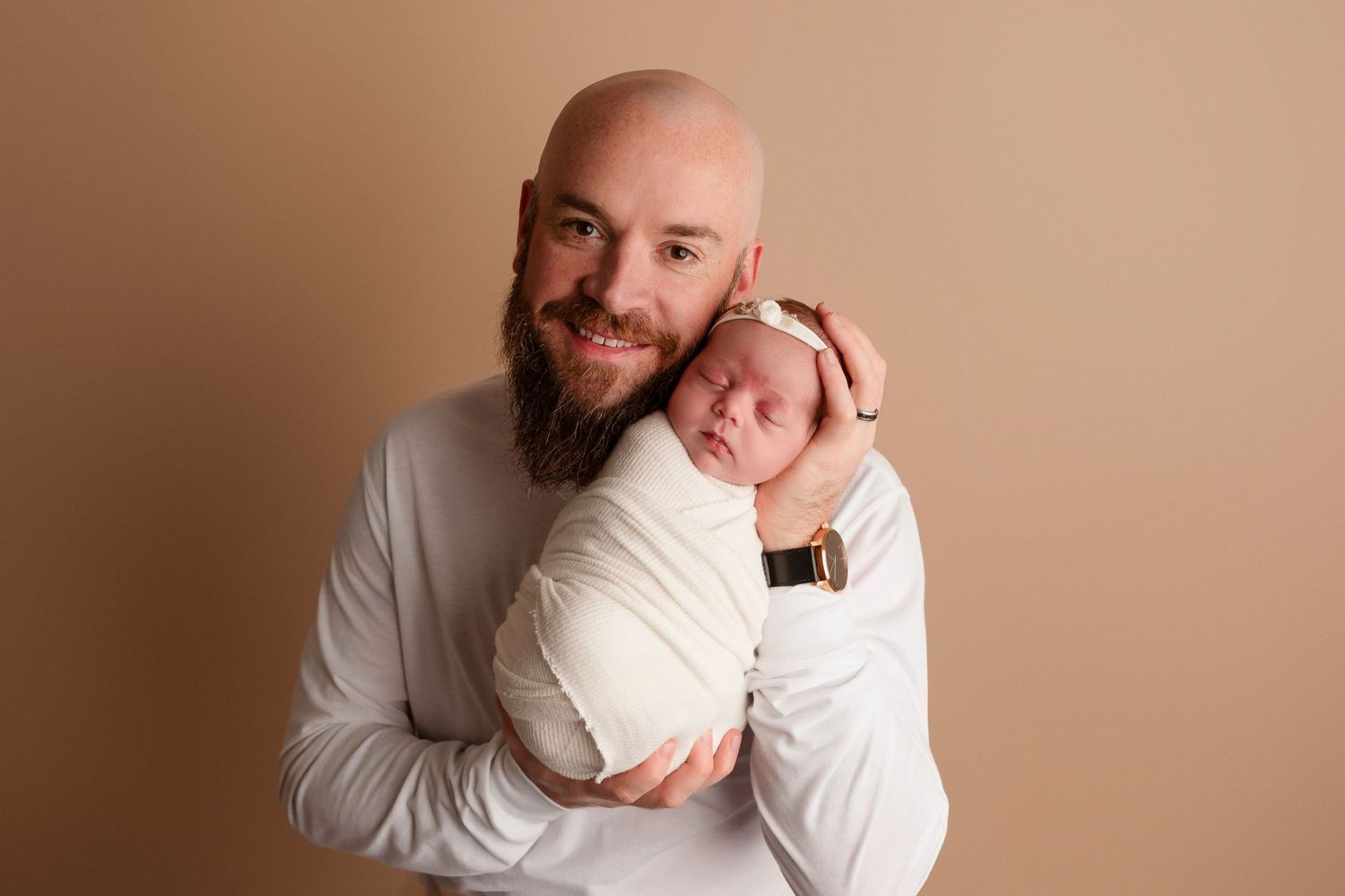 Tender newborn photography session with parent and baby against warm beige backdrop.
