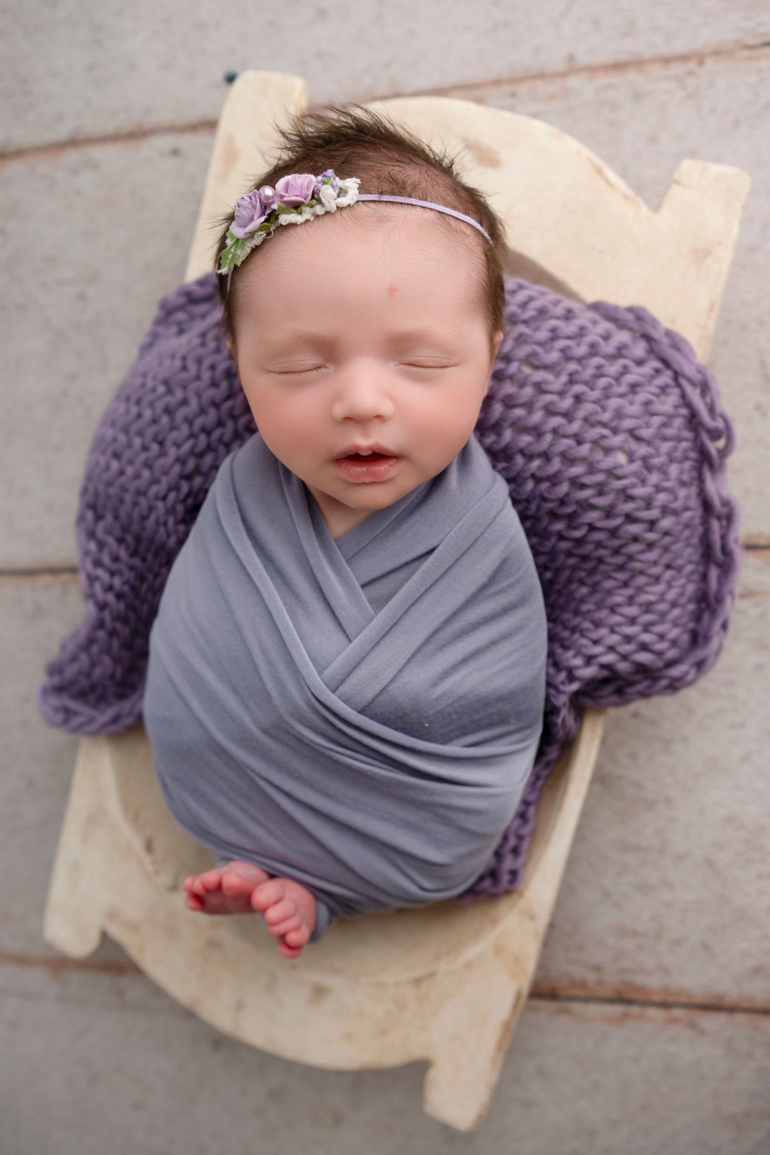 Newborn photography series featuring baby wrapped in grey fabric with purple knit blanket on wooden floor.