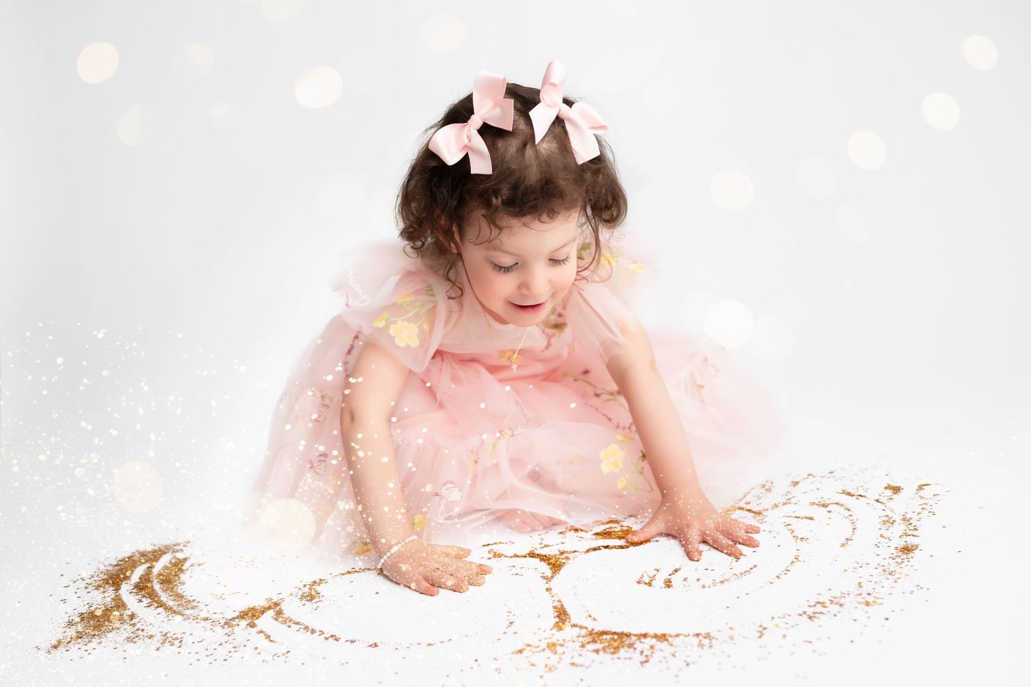 A child in a pink dress sits on the floor playing with gold glitter and confetti.