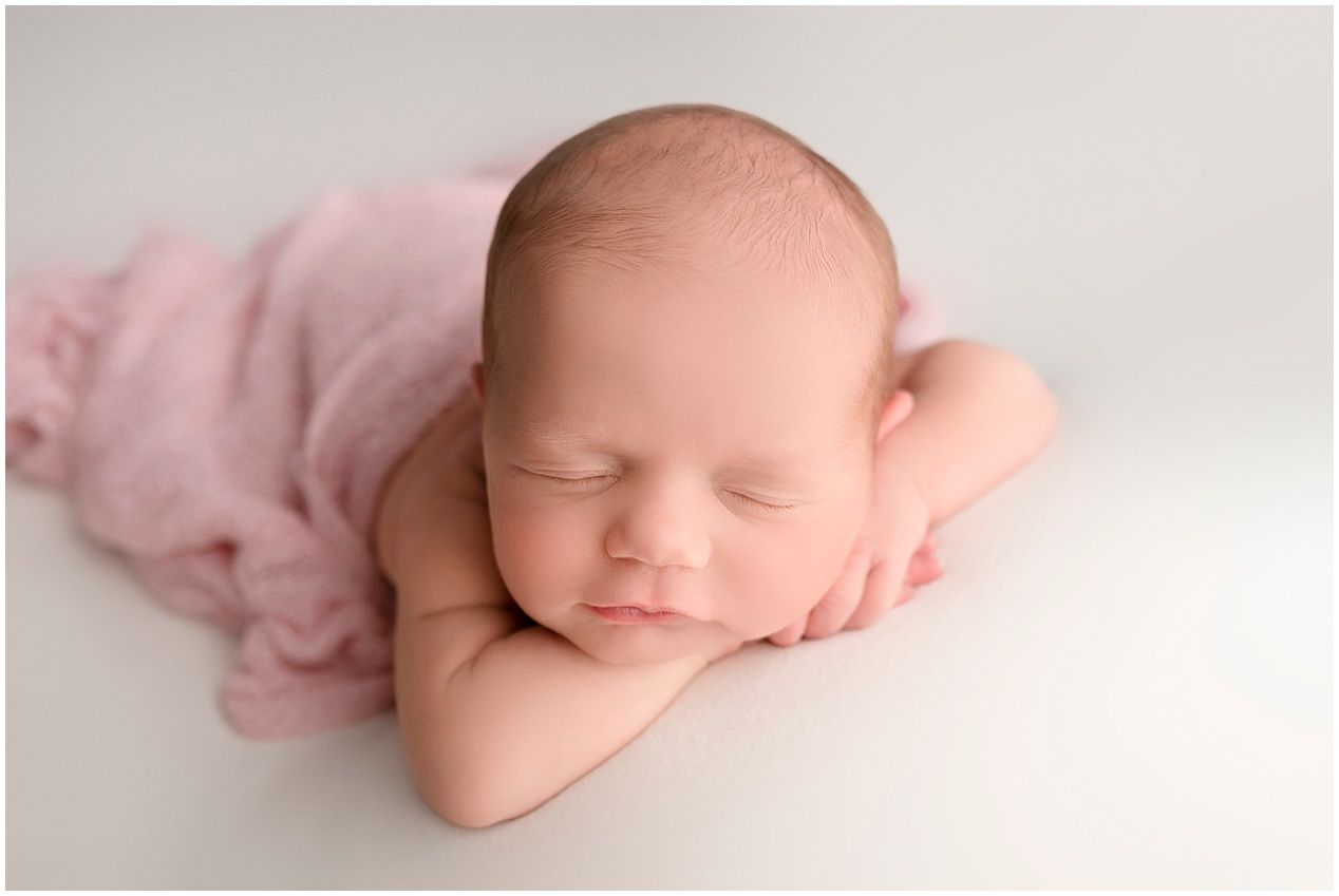A series of minimalist newborn baby photographs showing gentle poses against soft white and pink backgrounds.