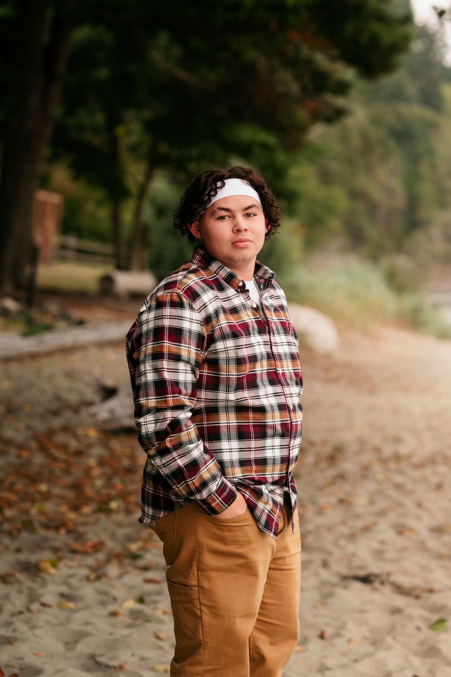 Multiple shots of a person in plaid flannel and brown pants posing on a wooded beach path.