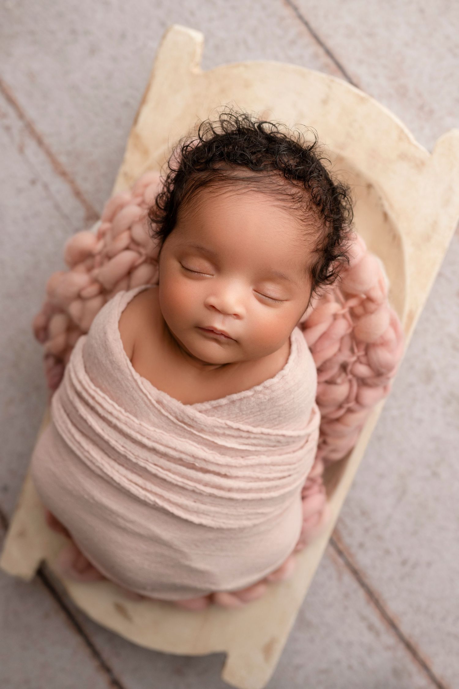 Newborn baby wrapped in soft pink fabric sleeping peacefully in professional photography setup.