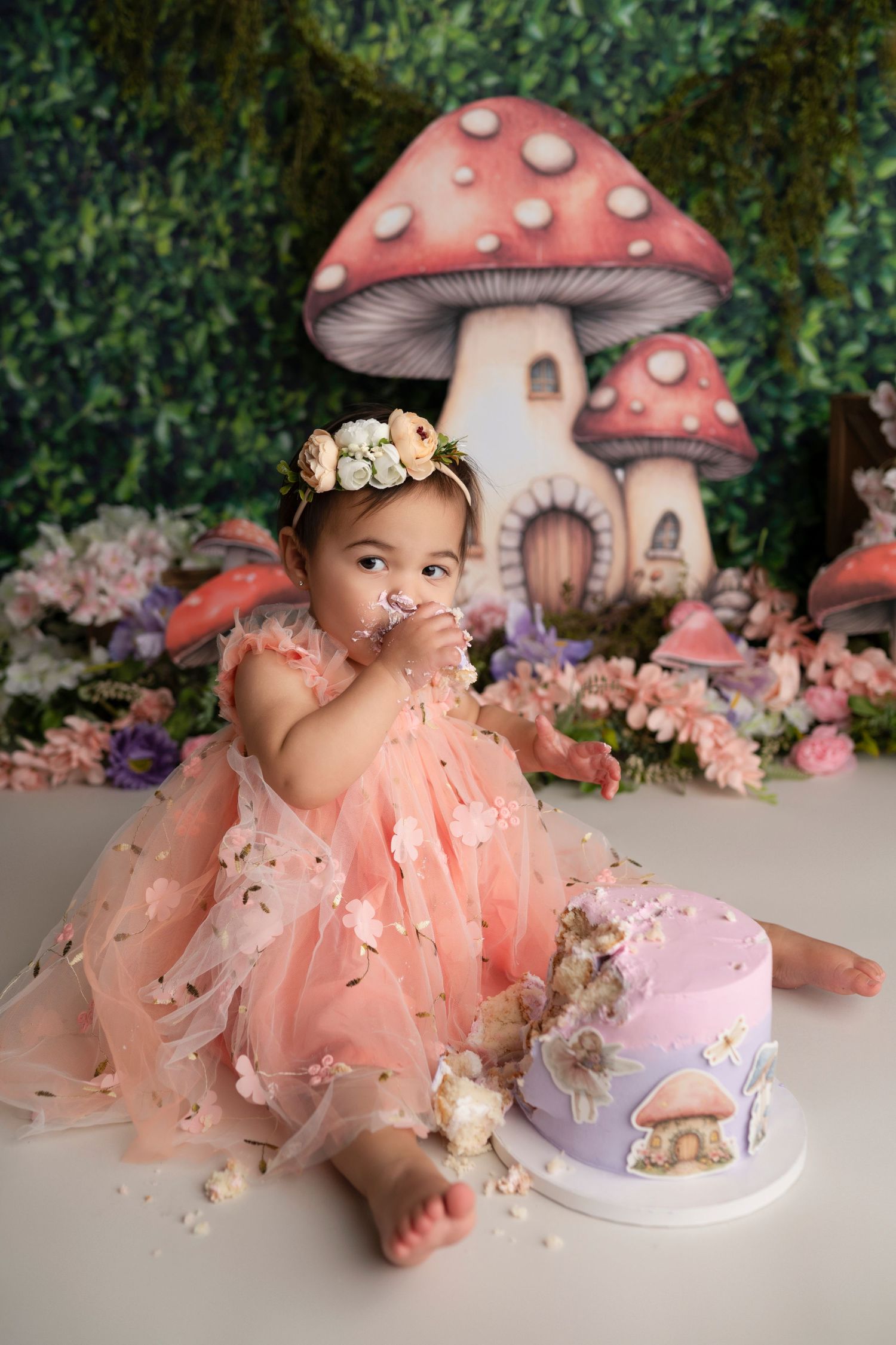 Whimsical fairy-themed photo setup with pink mushroom houses, flowers, and soft decorative elements.