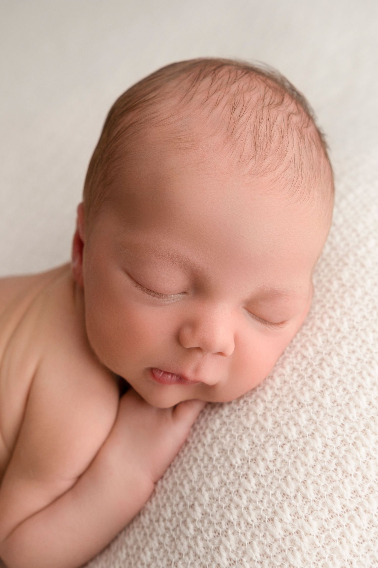 Peaceful sleeping newborn baby resting on soft white textured blanket in gentle natural light.