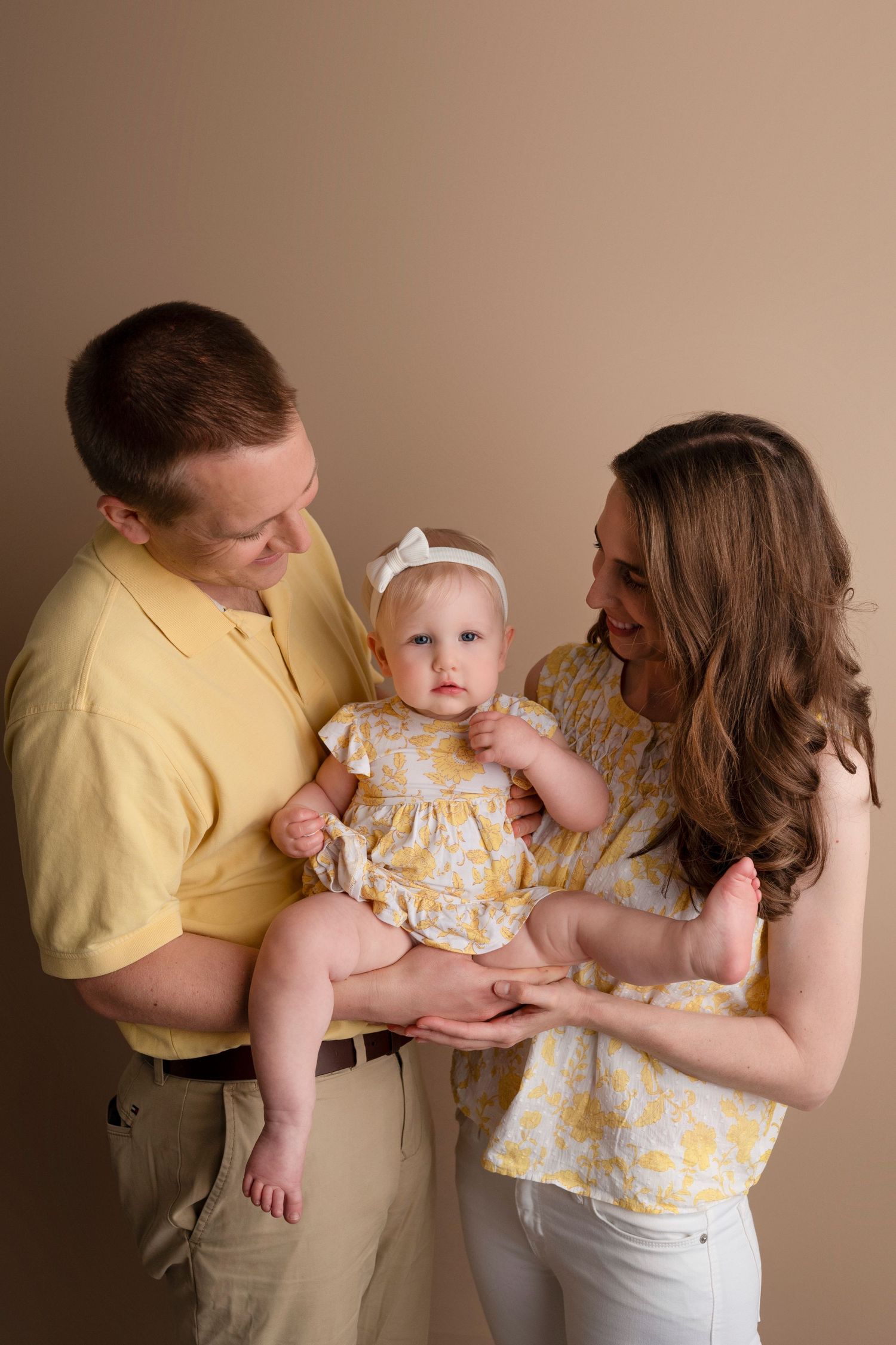 A series of candid family photos showing parents interacting with a baby in a yellow dress against a neutral background.