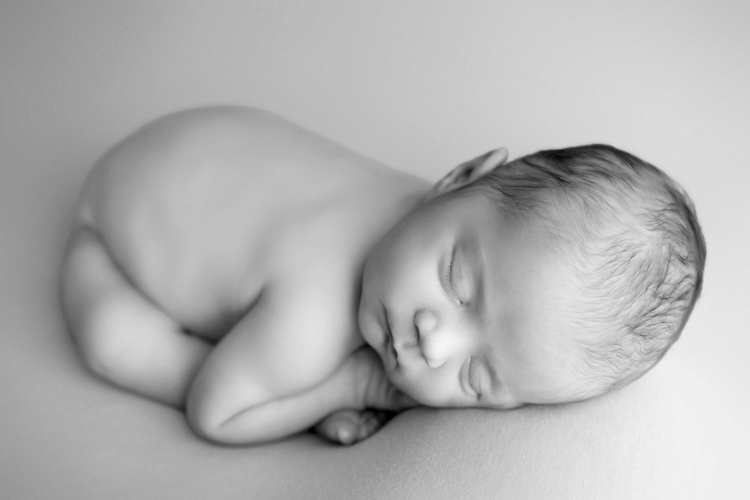 Black and white newborn baby sleeping peacefully curled up, serene infant portrait photography.