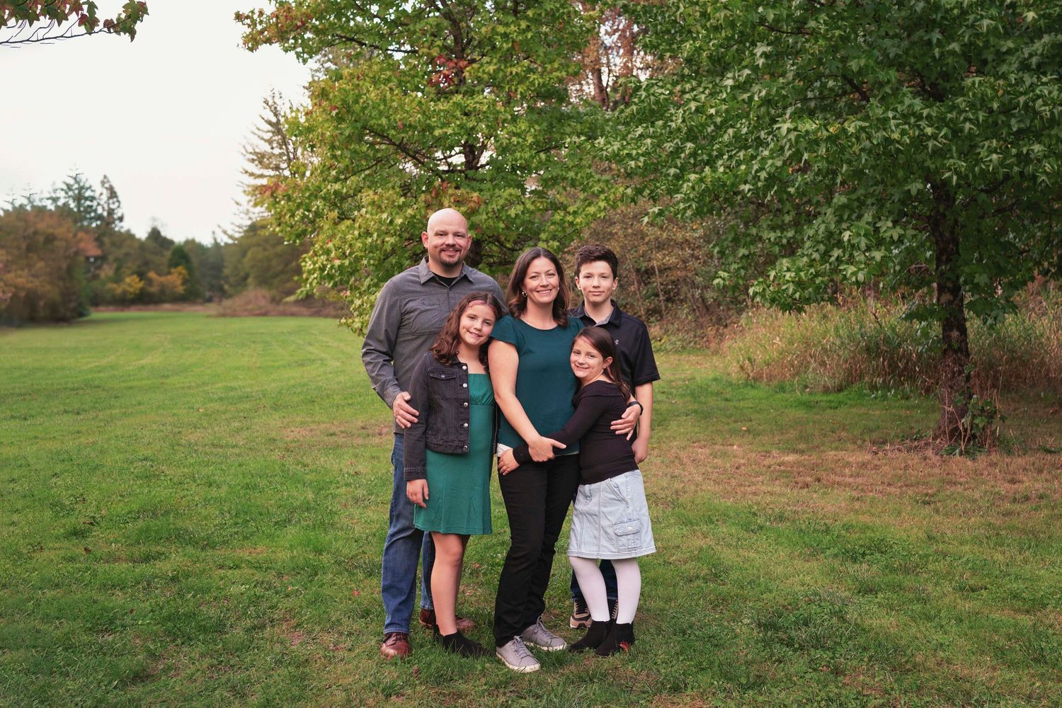 Family poses together on grassy hillside during autumn outdoor photo session.