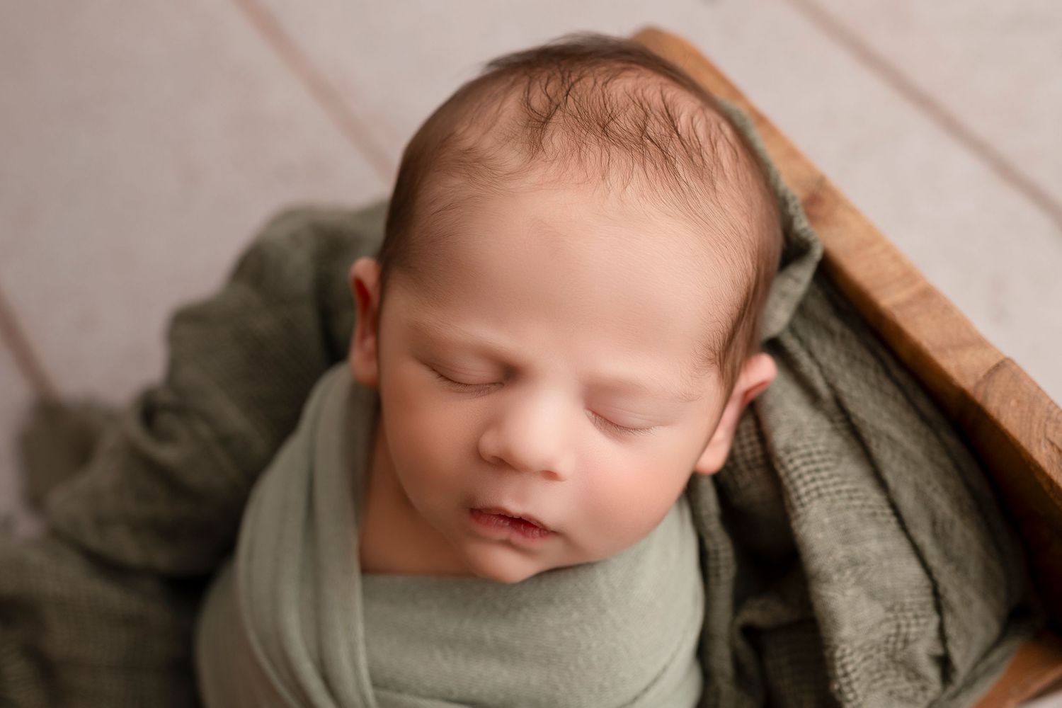 Collection of artistic newborn portraits with soft neutral wrapping against rustic wooden background.