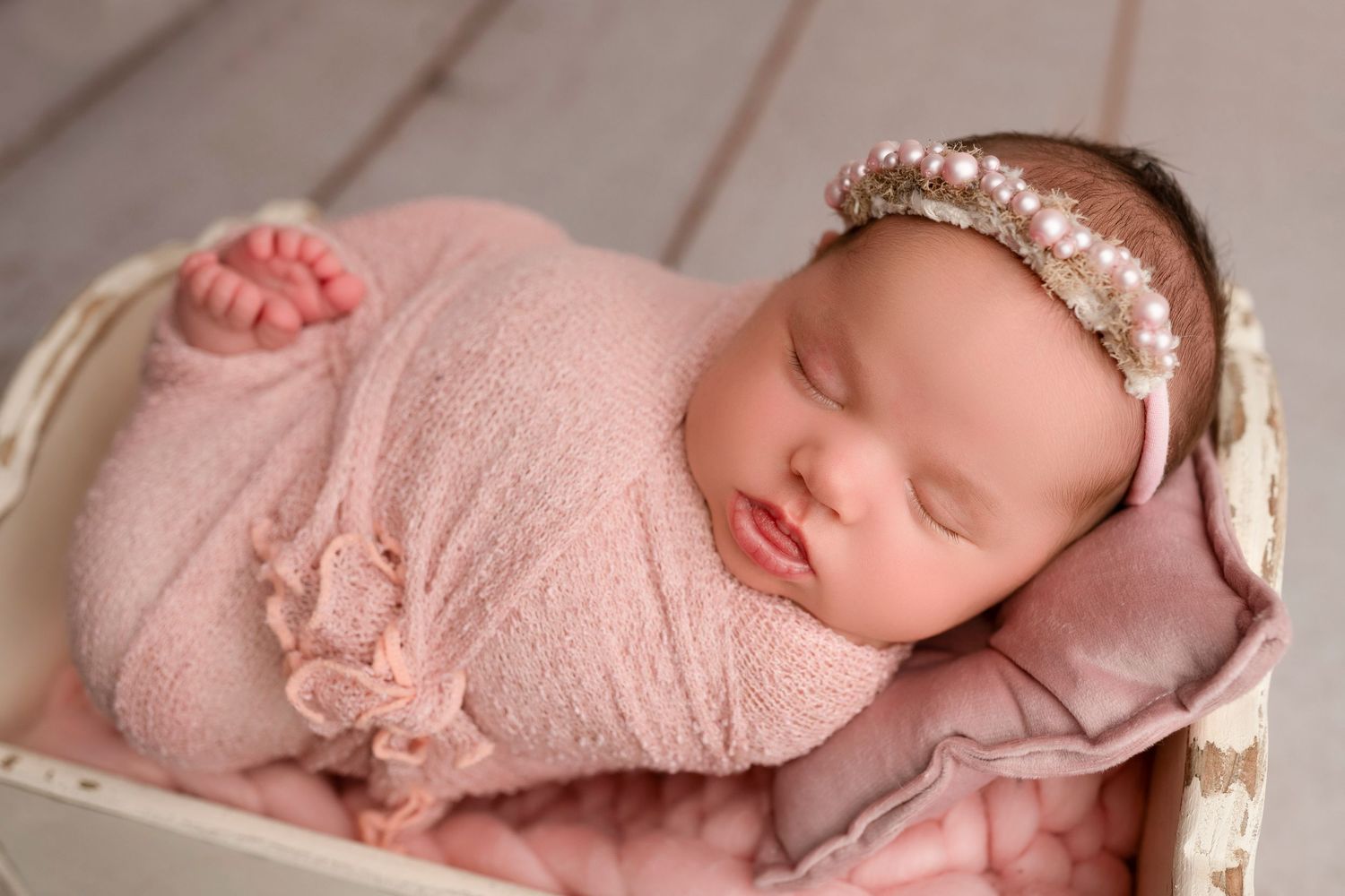 Sleeping newborn baby wrapped in soft pink blanket during professional photography session.