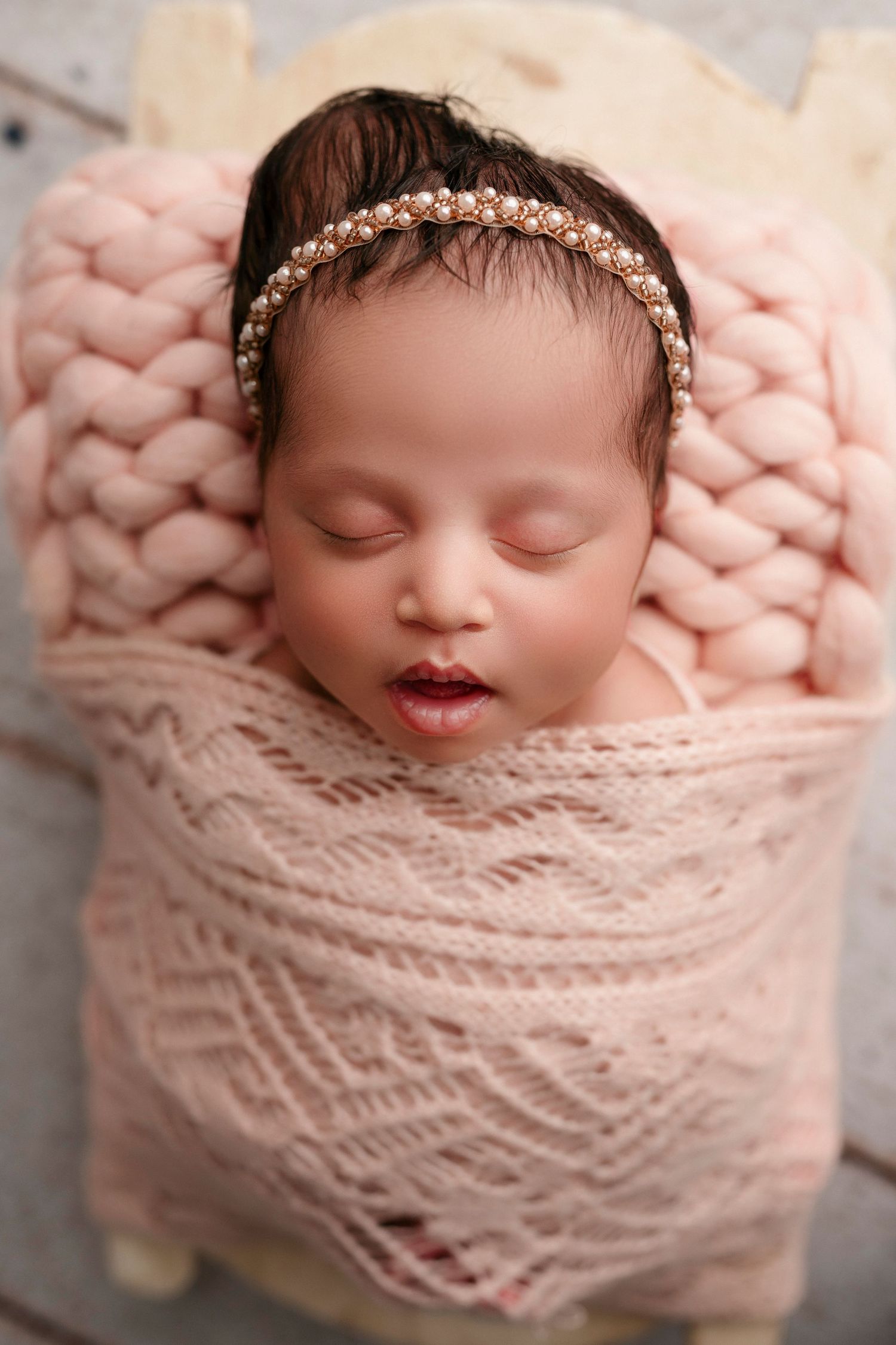Sleeping newborn baby wrapped in soft pink knitted blanket during professional photo session.