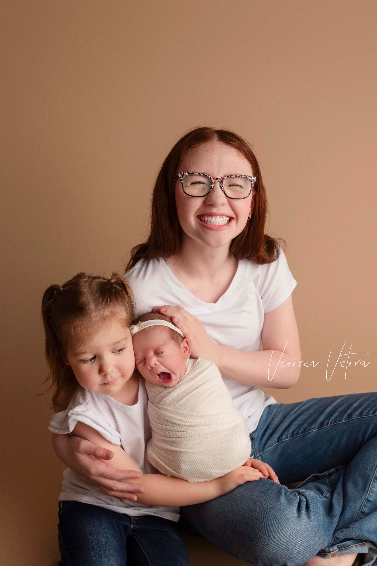 A series of intimate lifestyle photos showing tender moments between siblings and a newborn baby against a neutral backdrop.