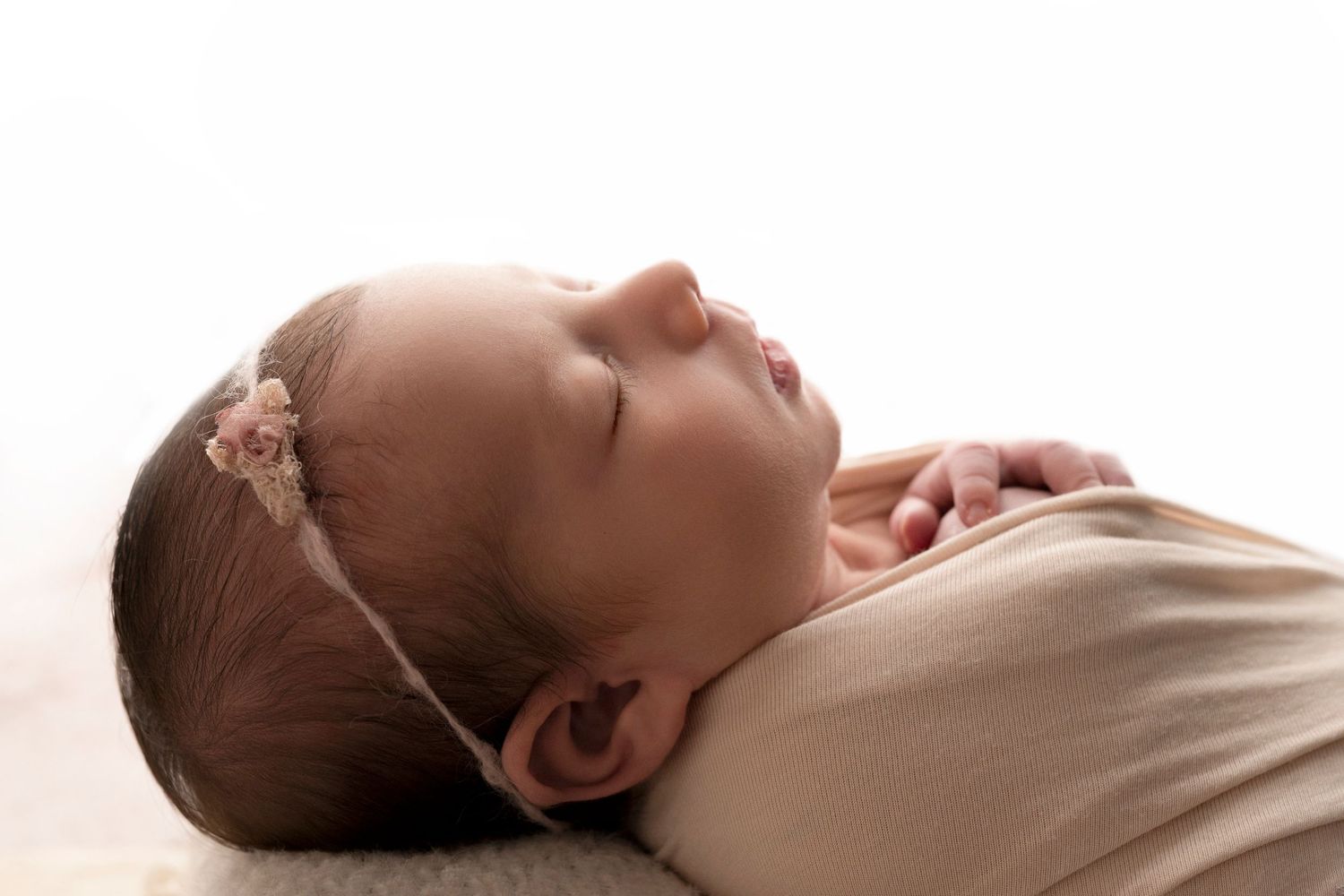Peaceful sleeping newborn baby girl wearing a delicate pink floral headband, swaddled in a soft wrap.