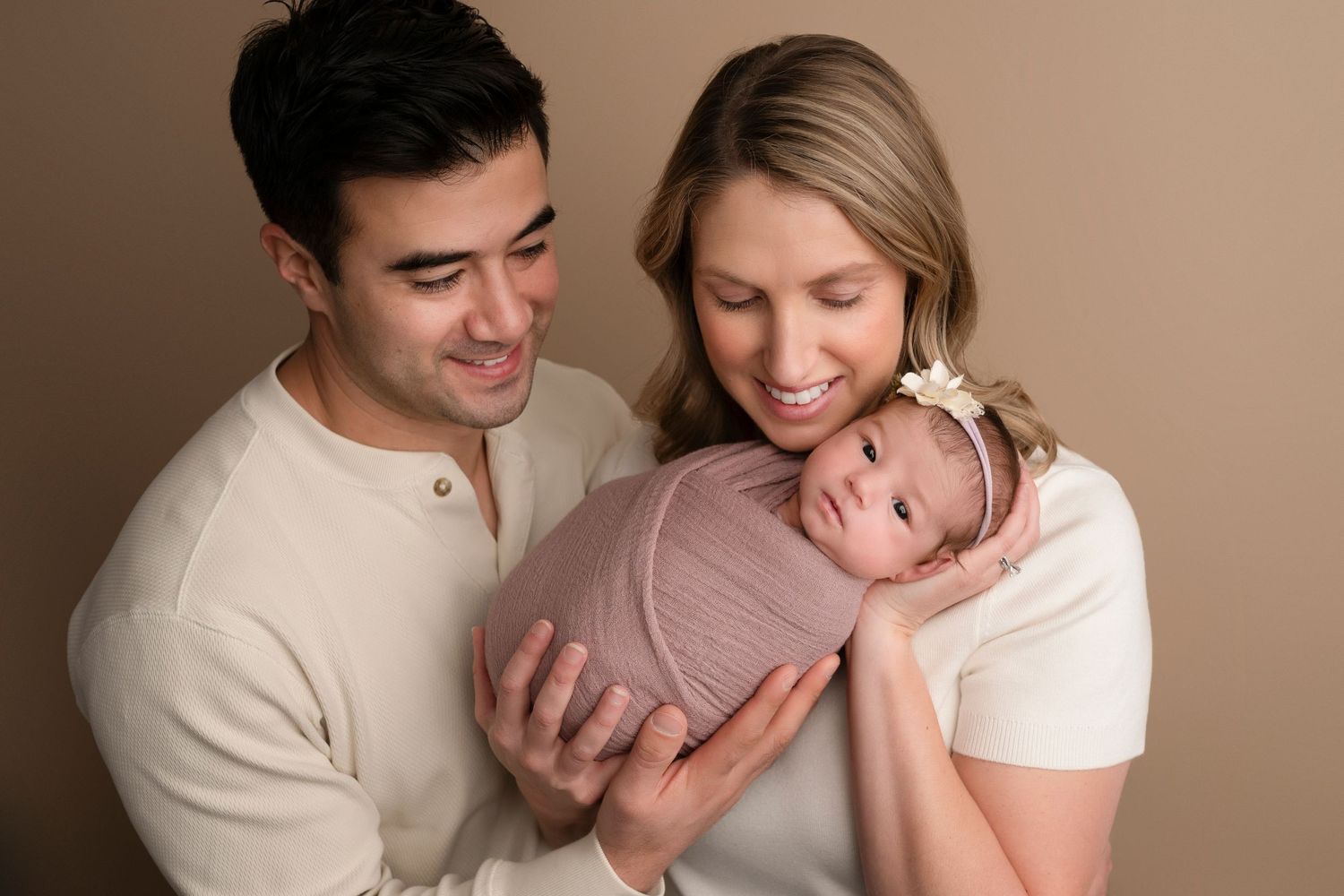 Parents smiling at their newborn baby wrapped in pink swaddle during professional newborn photography session.