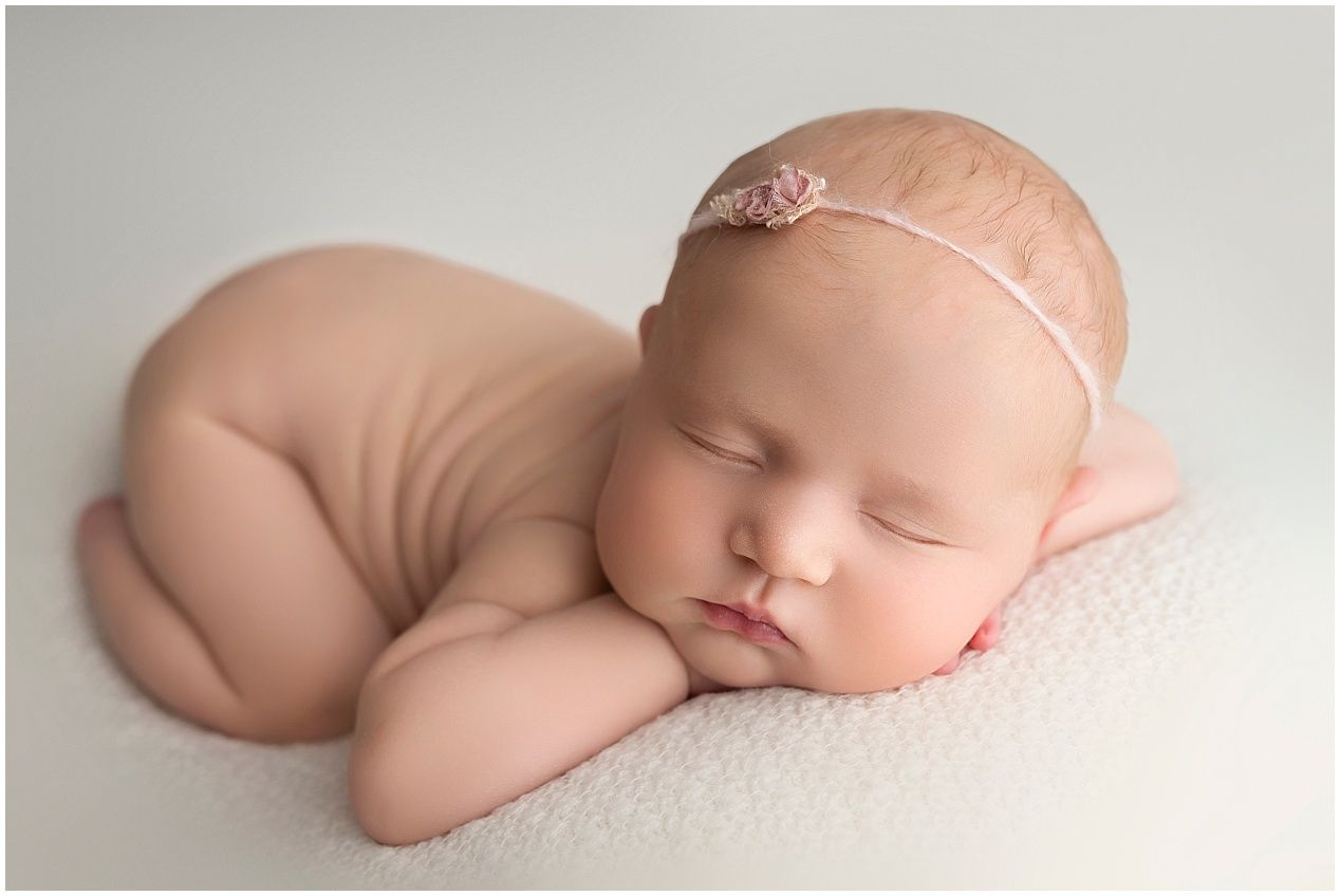 Peaceful sleeping newborn baby curled up on soft white backdrop wearing delicate headband.