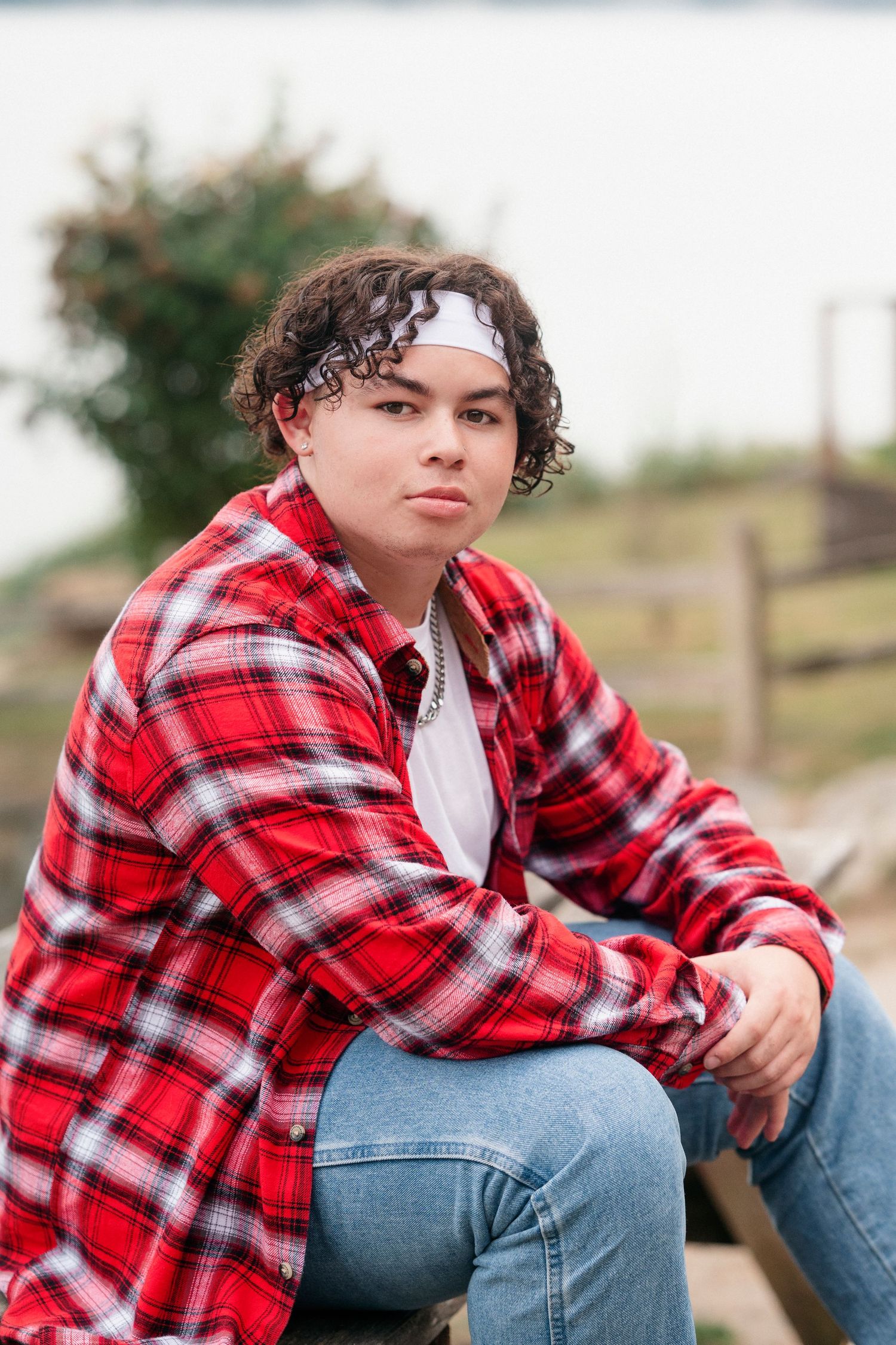 Someone in a red plaid flannel shirt and jeans sits casually outdoors in a series of casual poses.