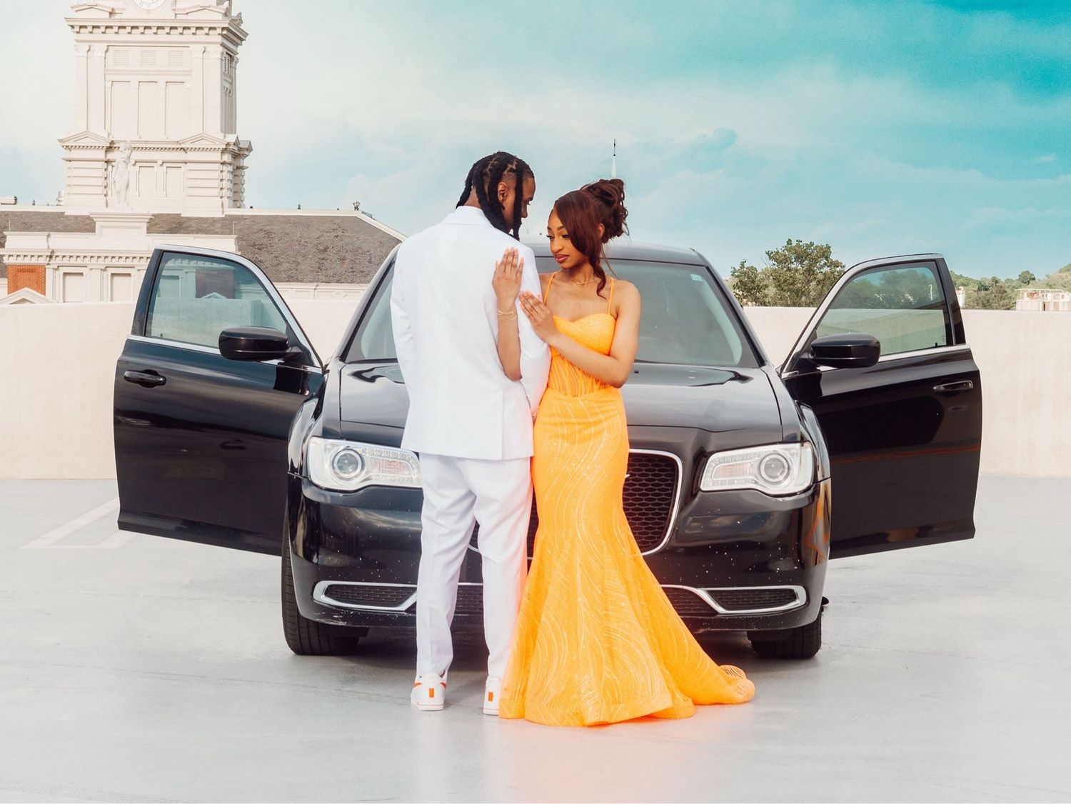 Elegant outdoor photoshoot featuring orange dress and luxury car.
