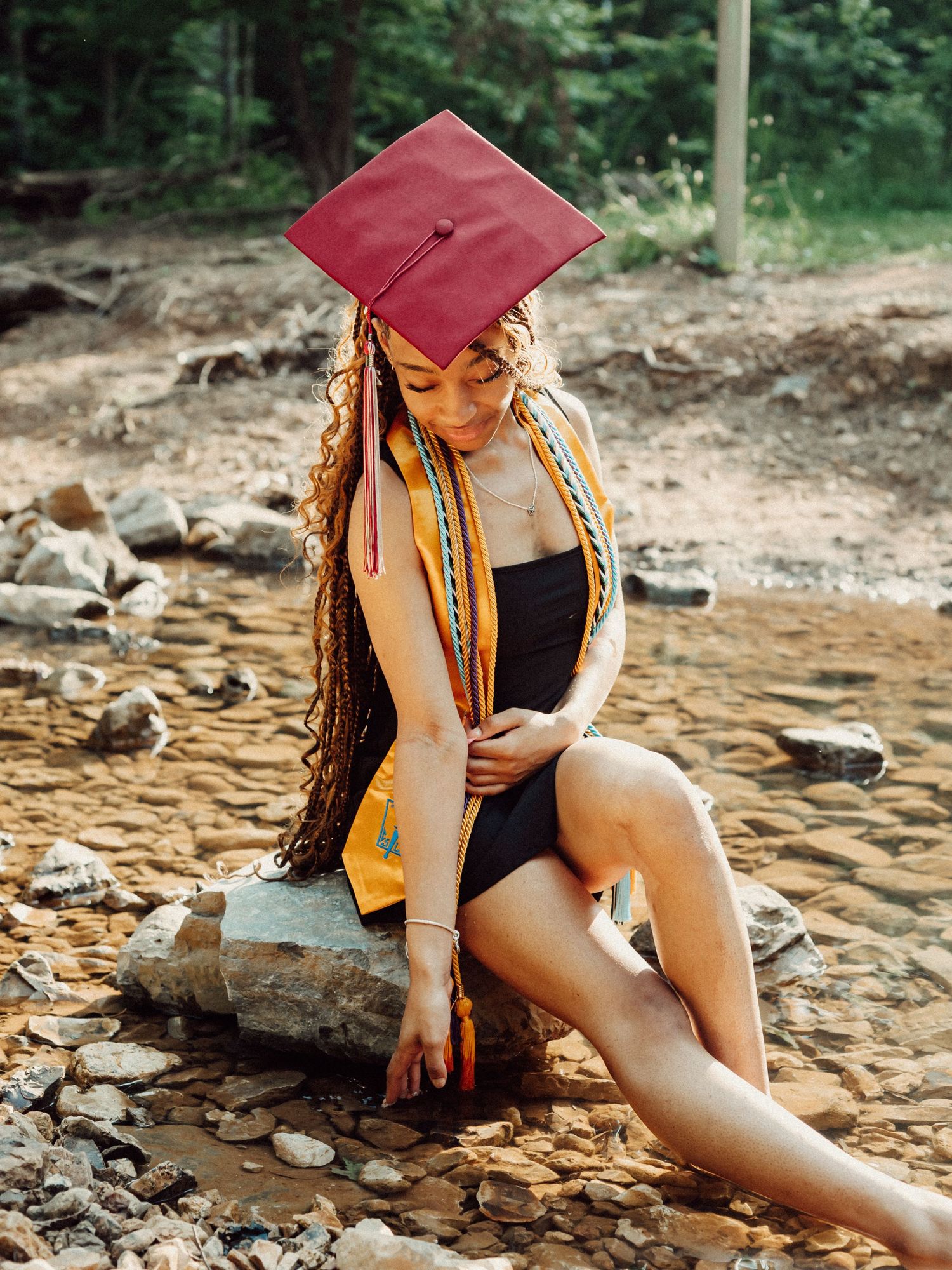 Graduation photos on rocky terrain wearing red cap and black outfit.
