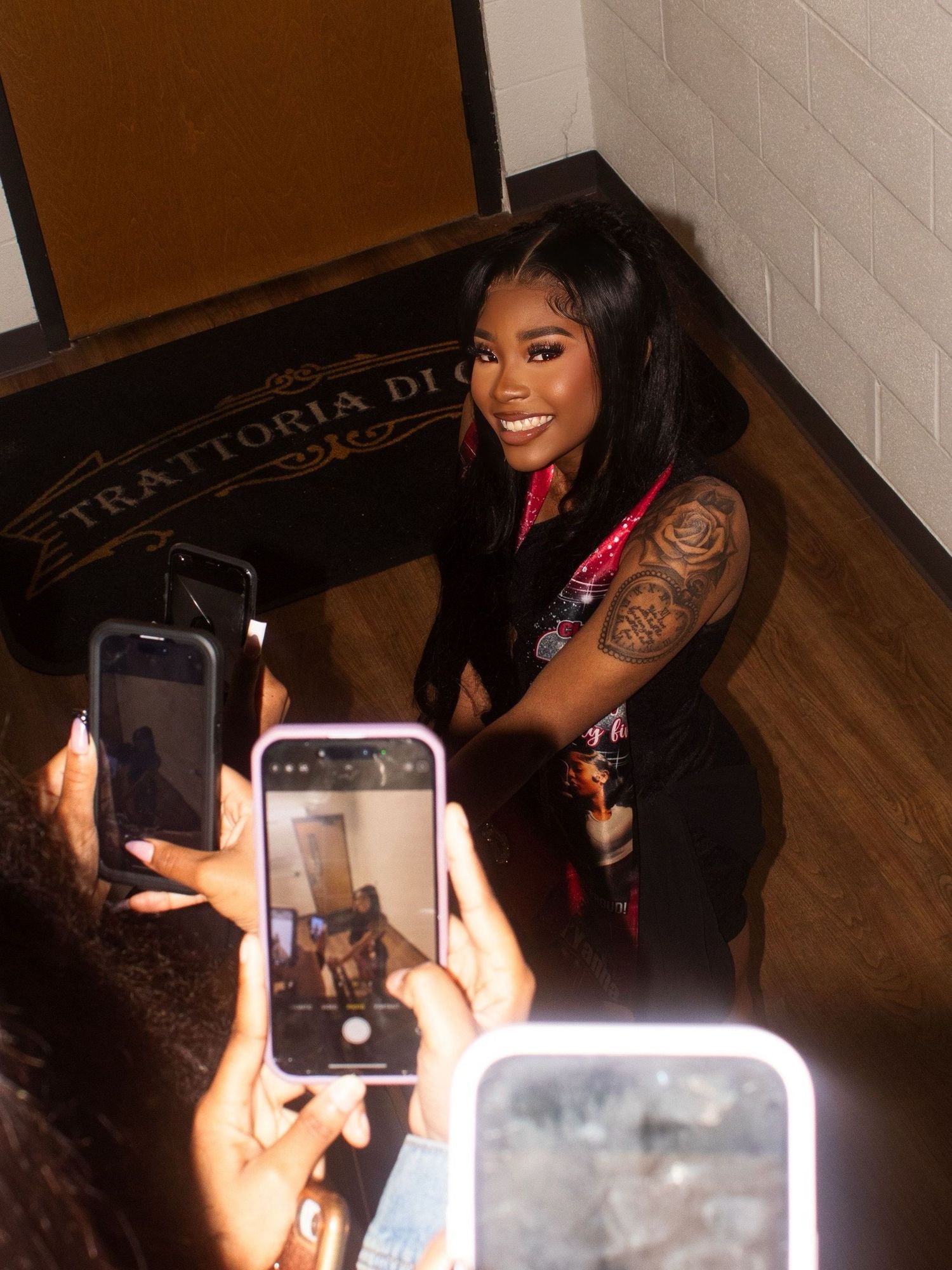 Multiple phones capturing photos at an indoor event with brick walls and dark lighting.