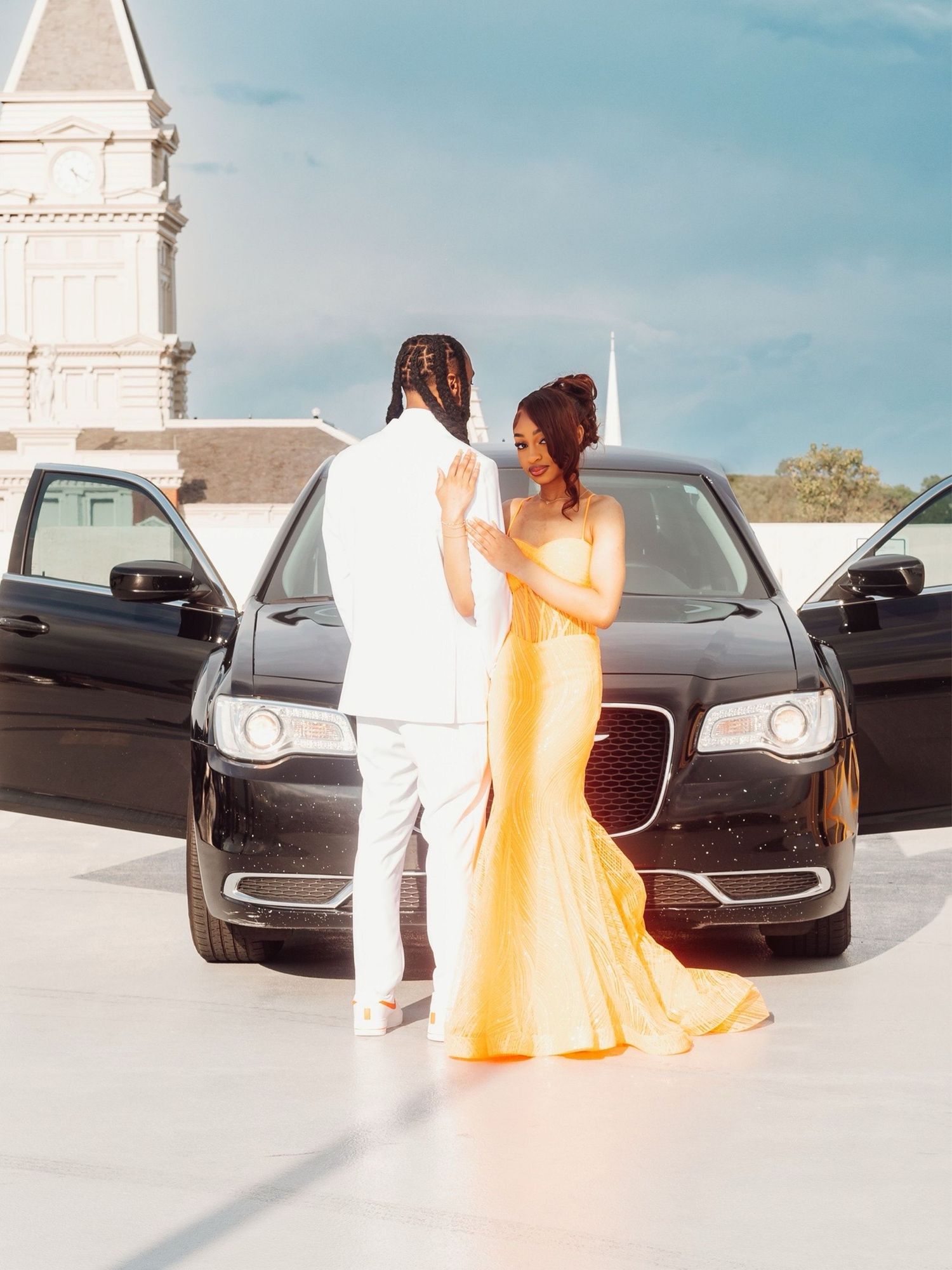 Outdoor photoshoot with orange formal dress and luxury vehicle.