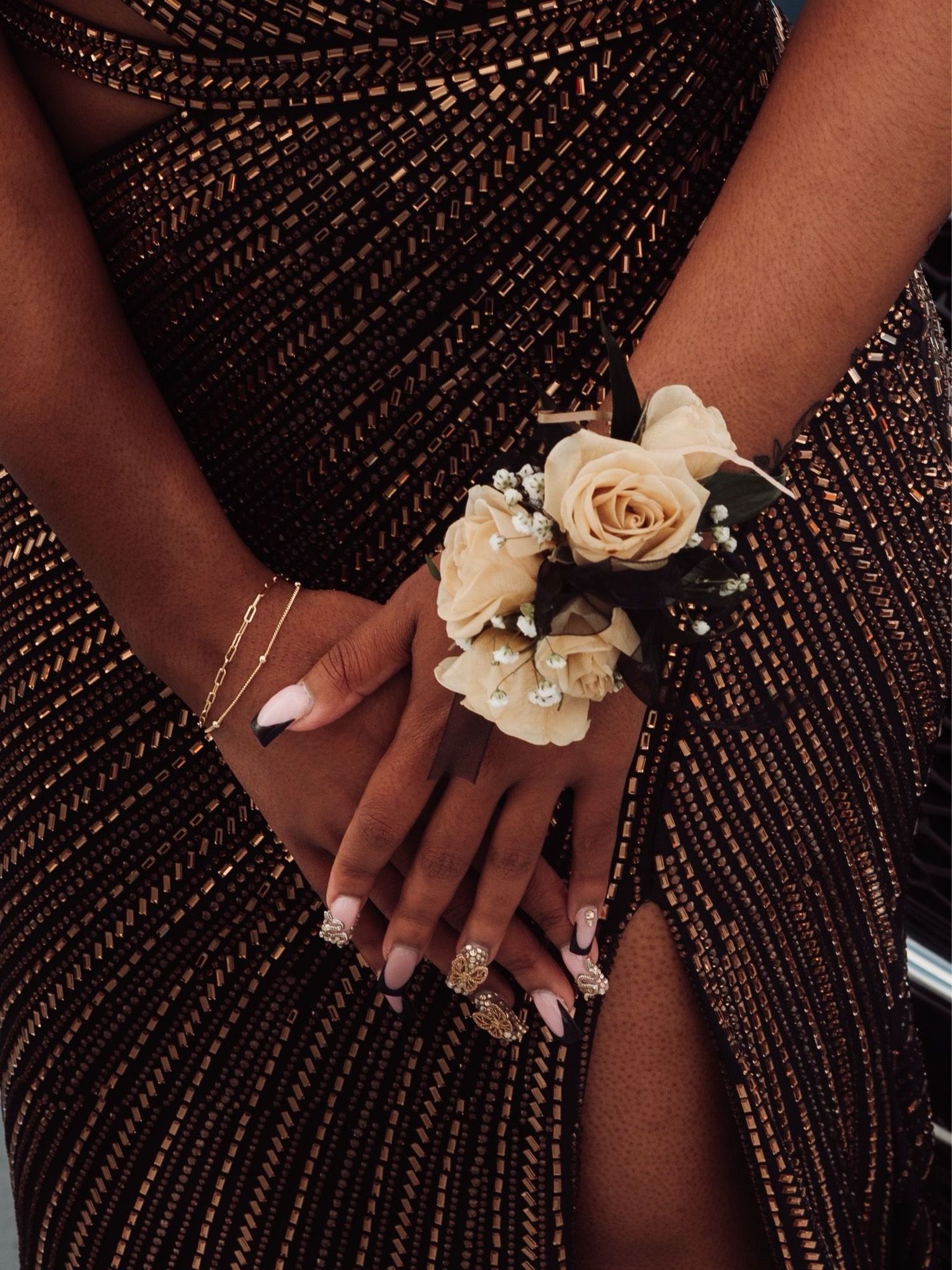 Close-up of hands wearing corsages against a sparkly brown formal dress fabric.