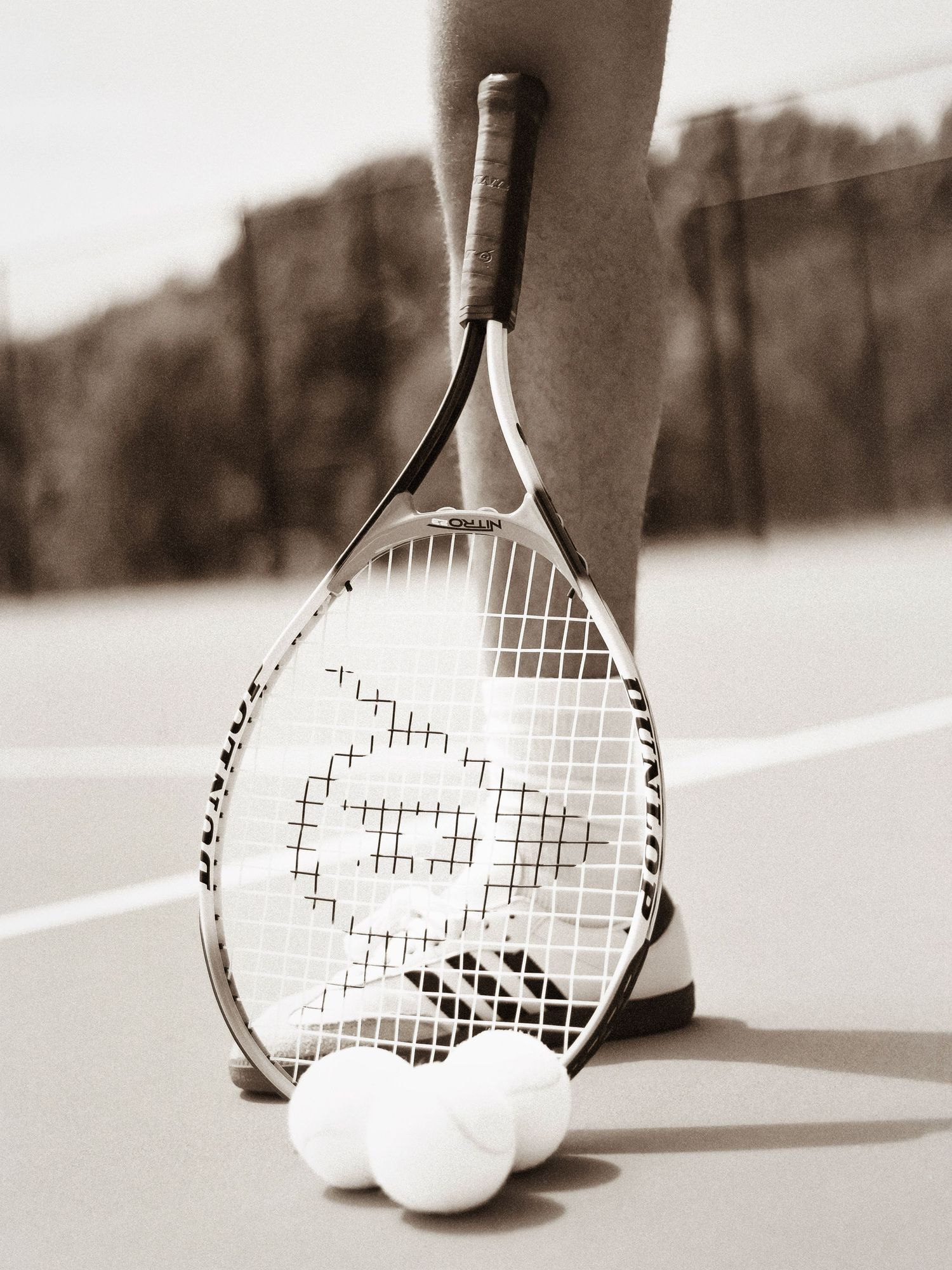 Black and white photo of tennis rackets creating shadows on a court surface.