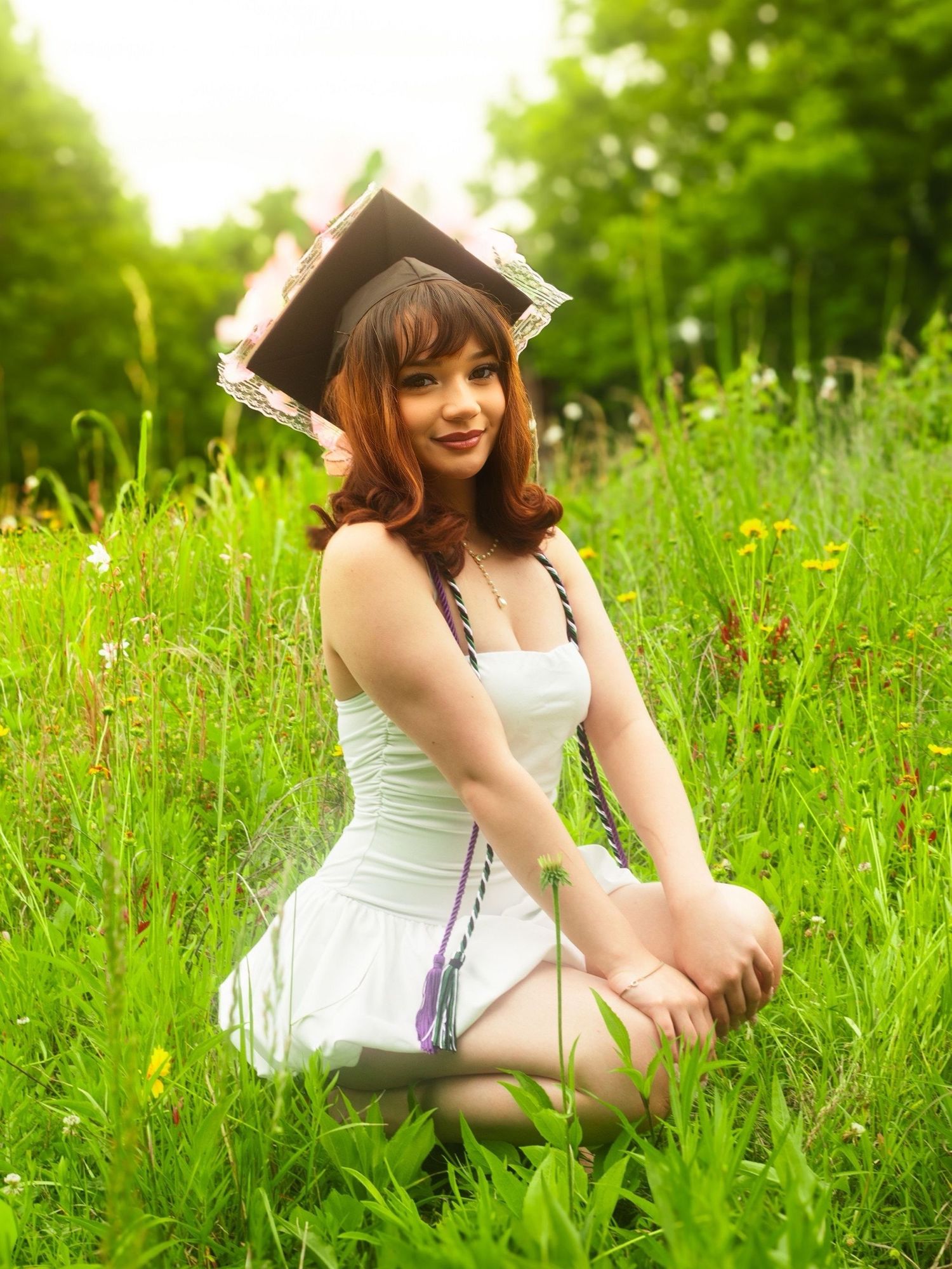 A person in a white dress and decorative headpiece poses gracefully in tall summer grass.