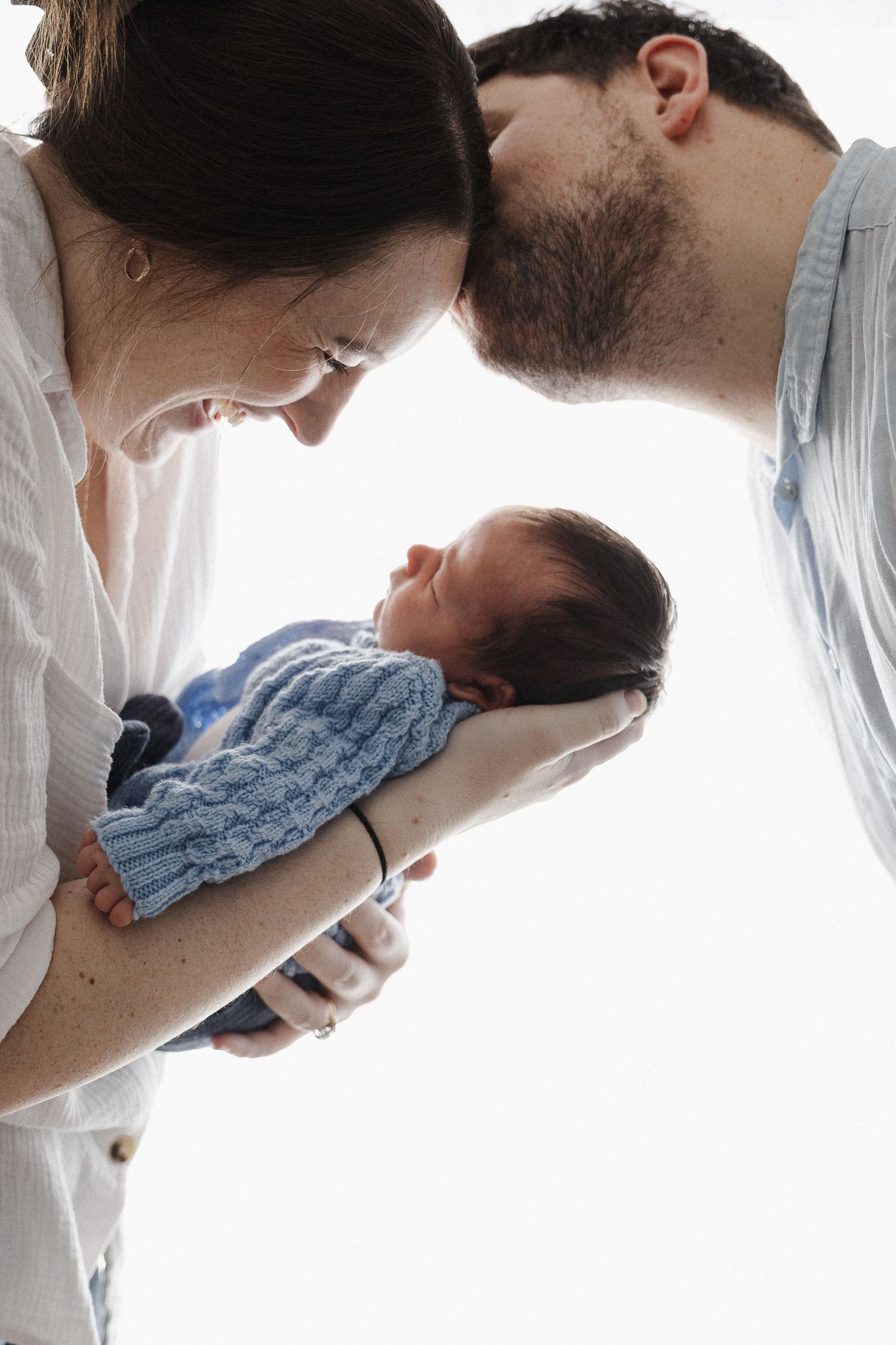 Dad kisses mum who looks at baby in newborn baby photoshoot in Canberra