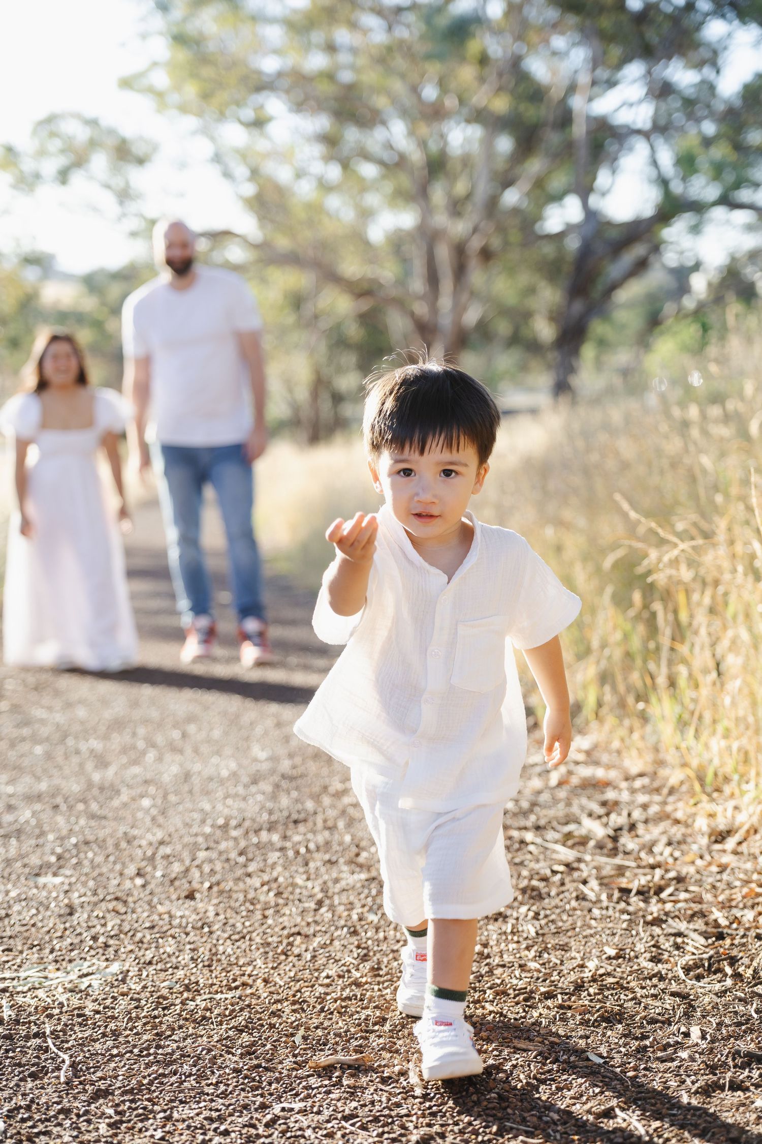Toddler runs toward the camera as his parents watch on in Canberra family photoshoot
