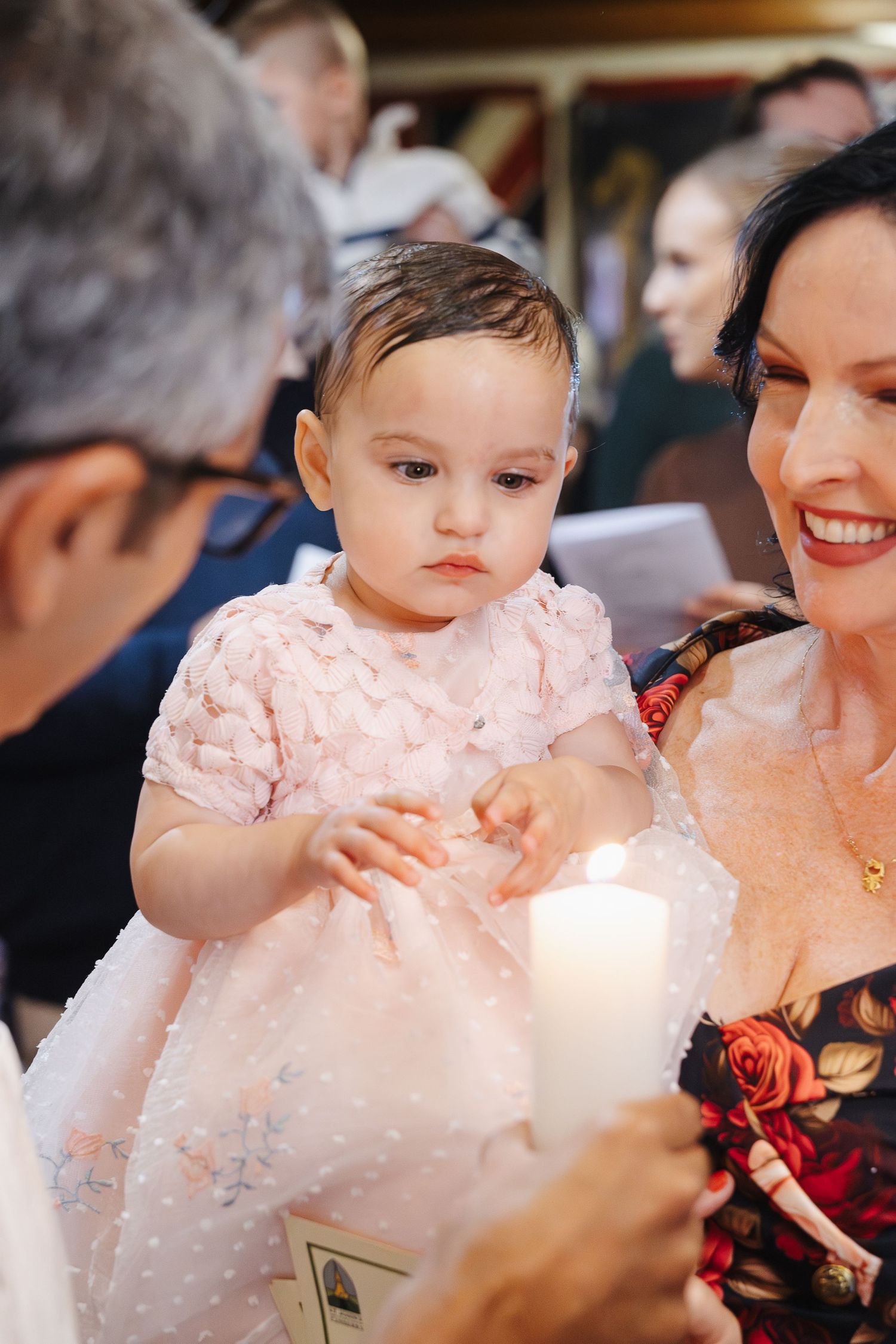 A newly-baptised baby girl looks at a candle with her parents