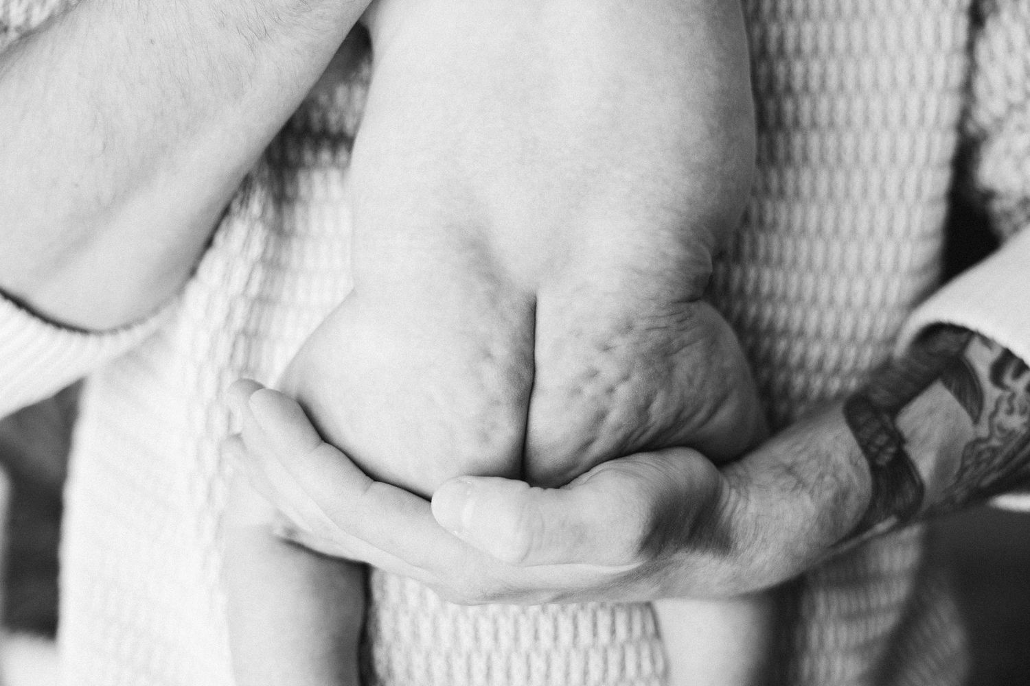 Black and white picture of naked newborn baby bottom in fathers hands in Belconnen Canberra photography studio