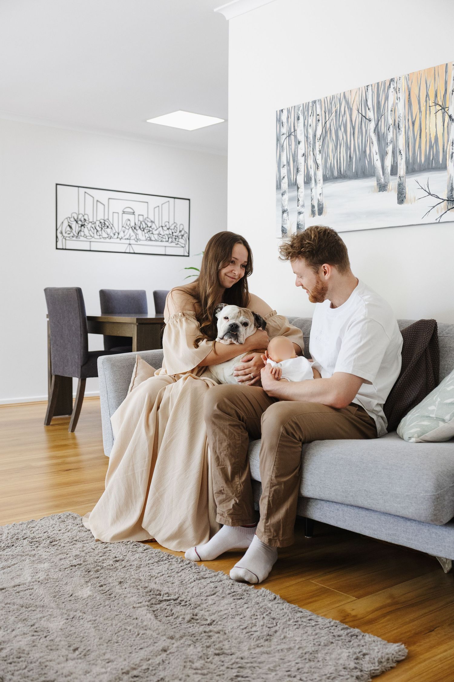 A couple laughs on the couch with their baby in a newborn photoshoot Canberra