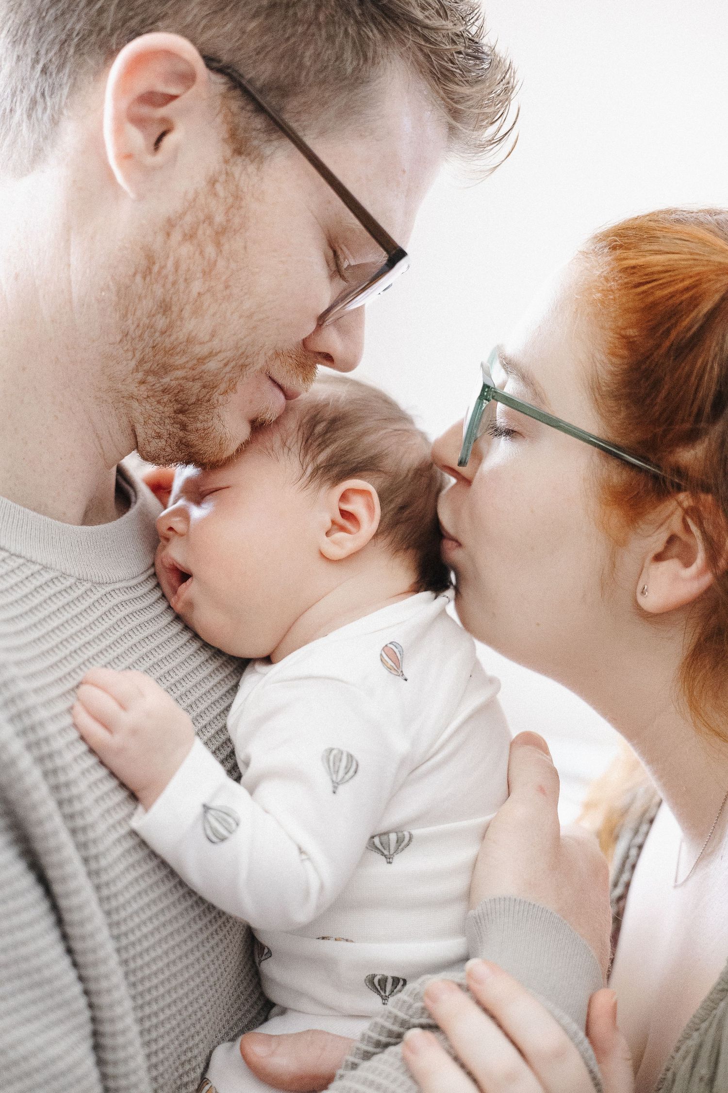 mum and dad kiss sleeping baby in newborn photoshoot canberra