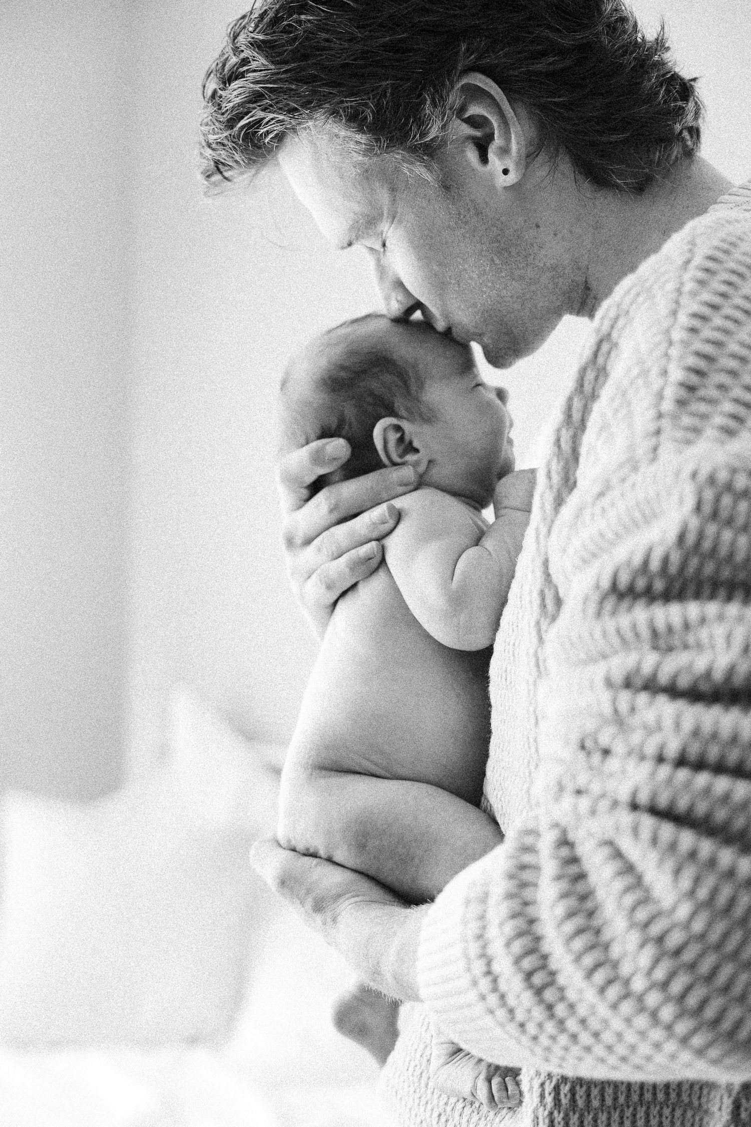 Black and white picture of father kissing his naked newborn baby in Belconnen Canberra photography studio