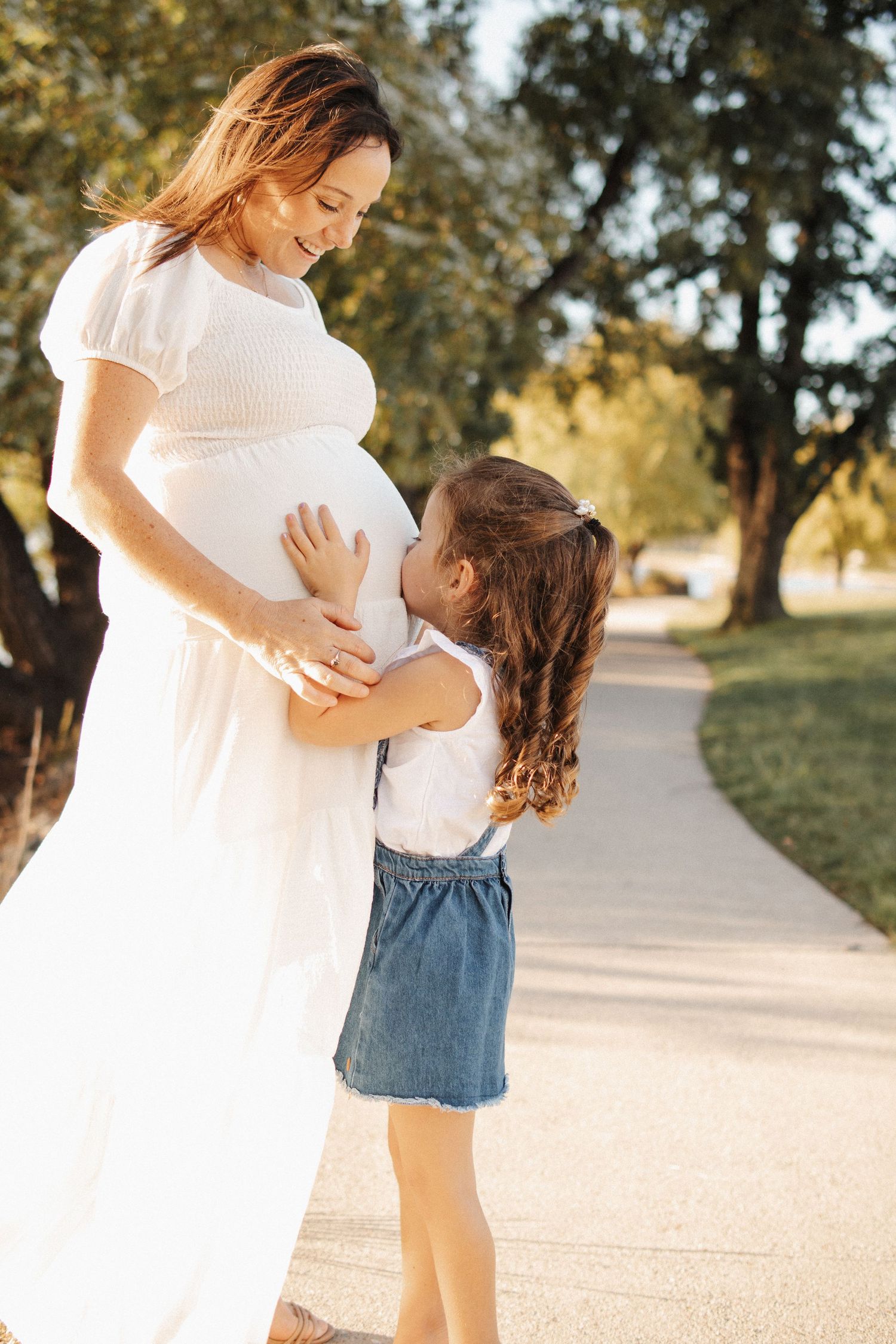 maternity photoshoot in Canberra with a little girl kissing her mother's pregnant belly
