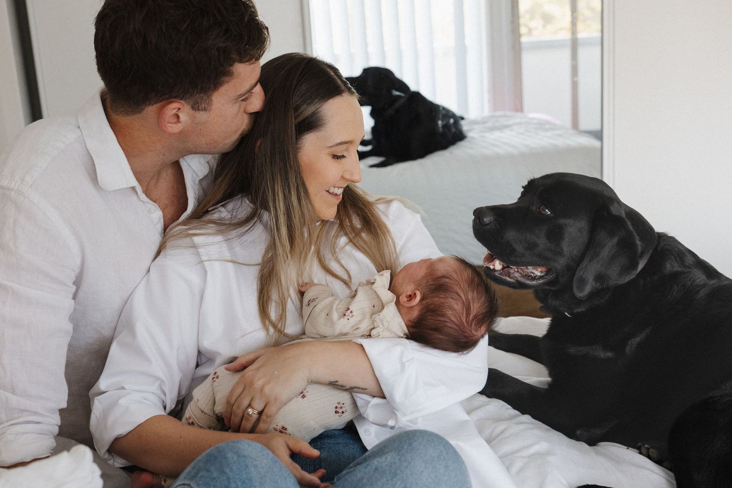 Parents cuddling their newborn baby on bed with their dog in Canberra