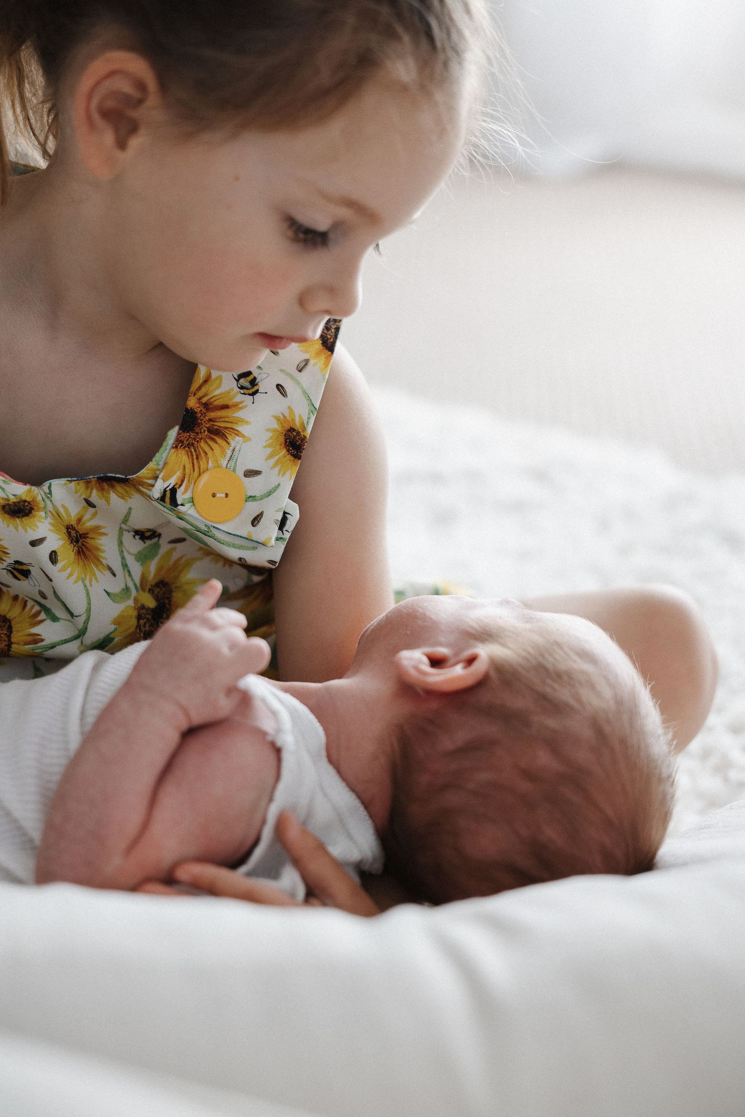 A big sister gazes at her baby brother in a newborn photoshoot with siblings in Canberra studio