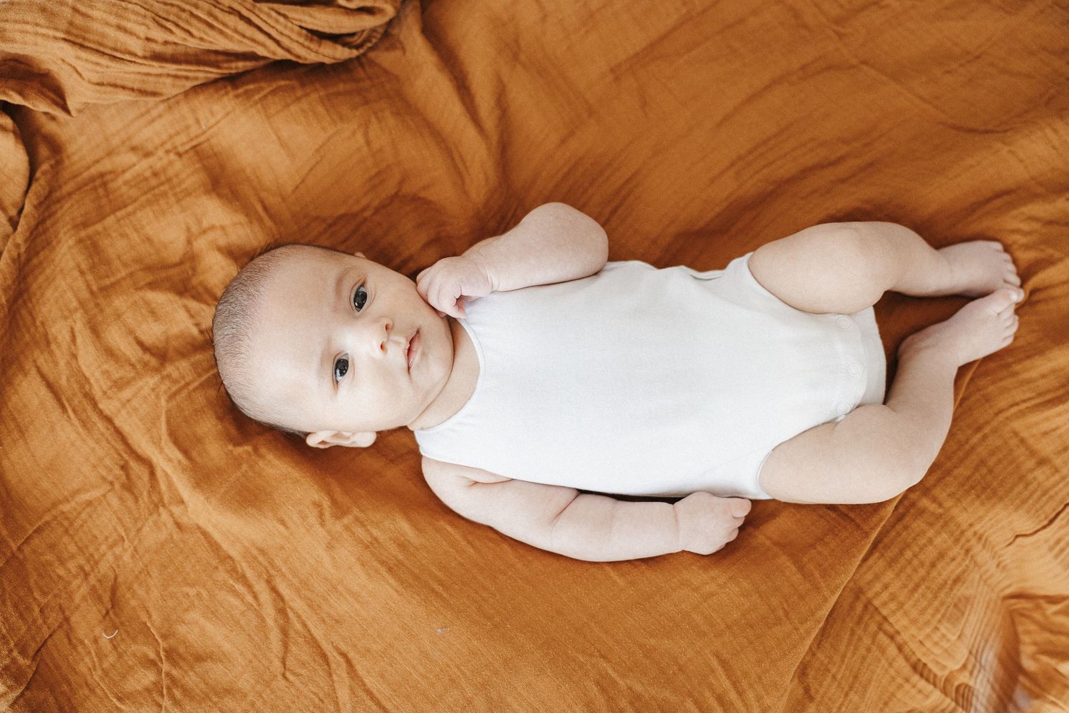Alert baby in singlet lying on bed in Belconnen Canberra photography studio