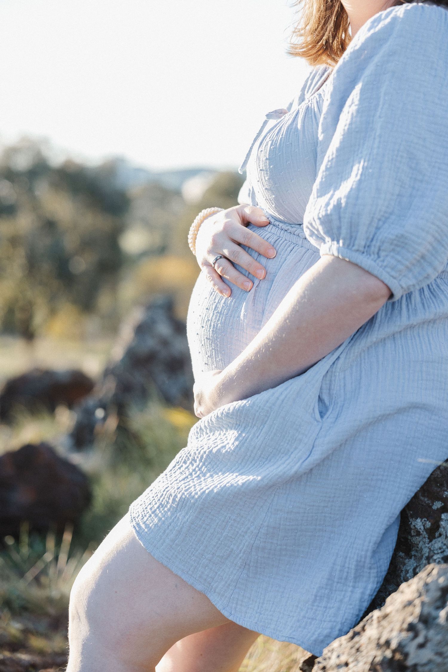 A woman rests her hand on her pregnant belly in a maternity photoshoot outdoors in Canberra