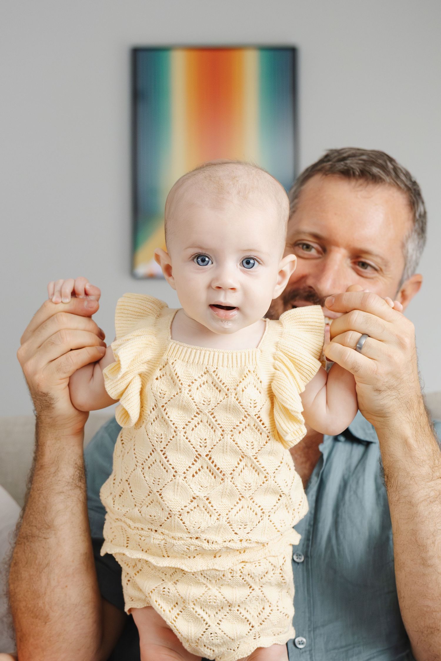 Baby standing on dad's lap during a family photoshoot in her Canberra home