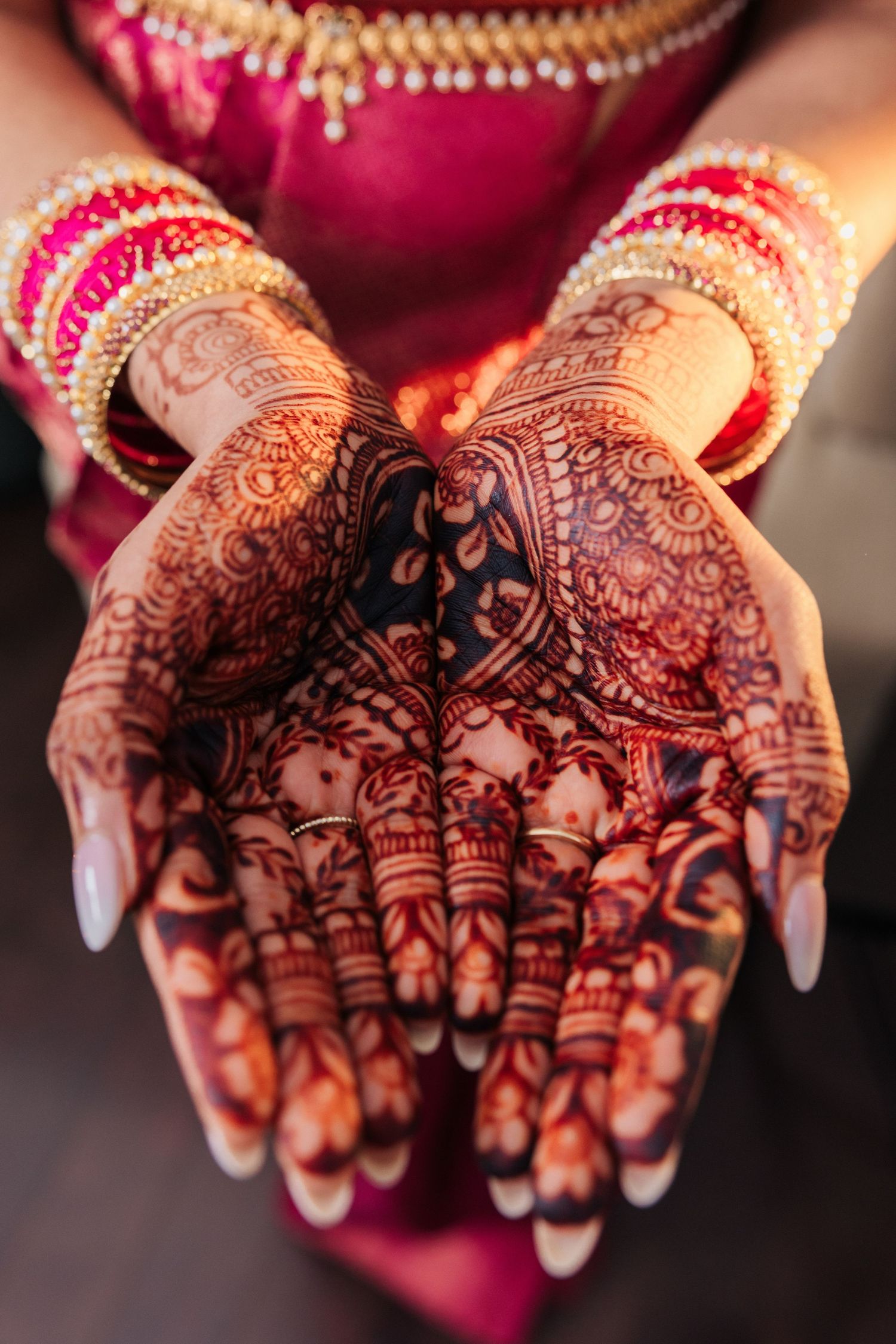 Bride's hands adorned with intricate henna mehndi designs and gold bangles in traditional Indian bridal style.