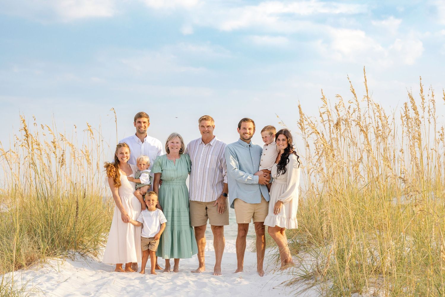 Extended family enjoying a summer day together at a beach with tall grass and sand dunes in the background.