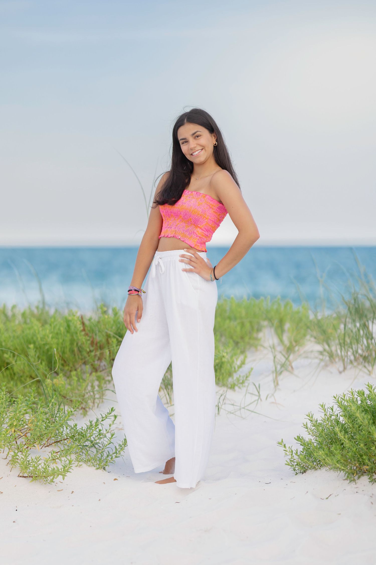 Woman in beach attire poses playfully on white sand with ocean in background.