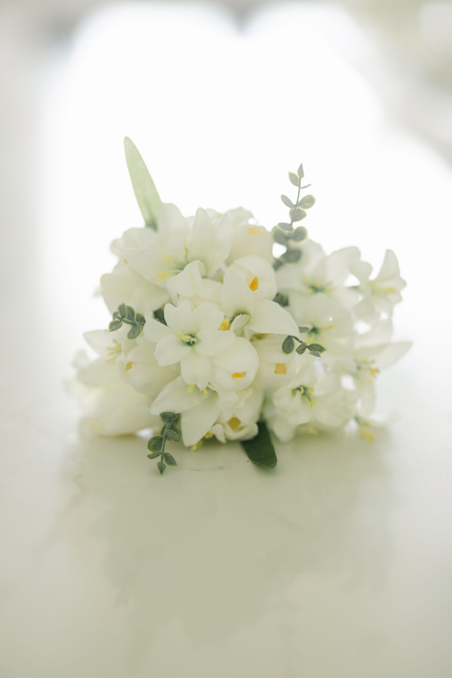 Elegant white floral bouquet with delicate greenery arranged against a soft blurred background.