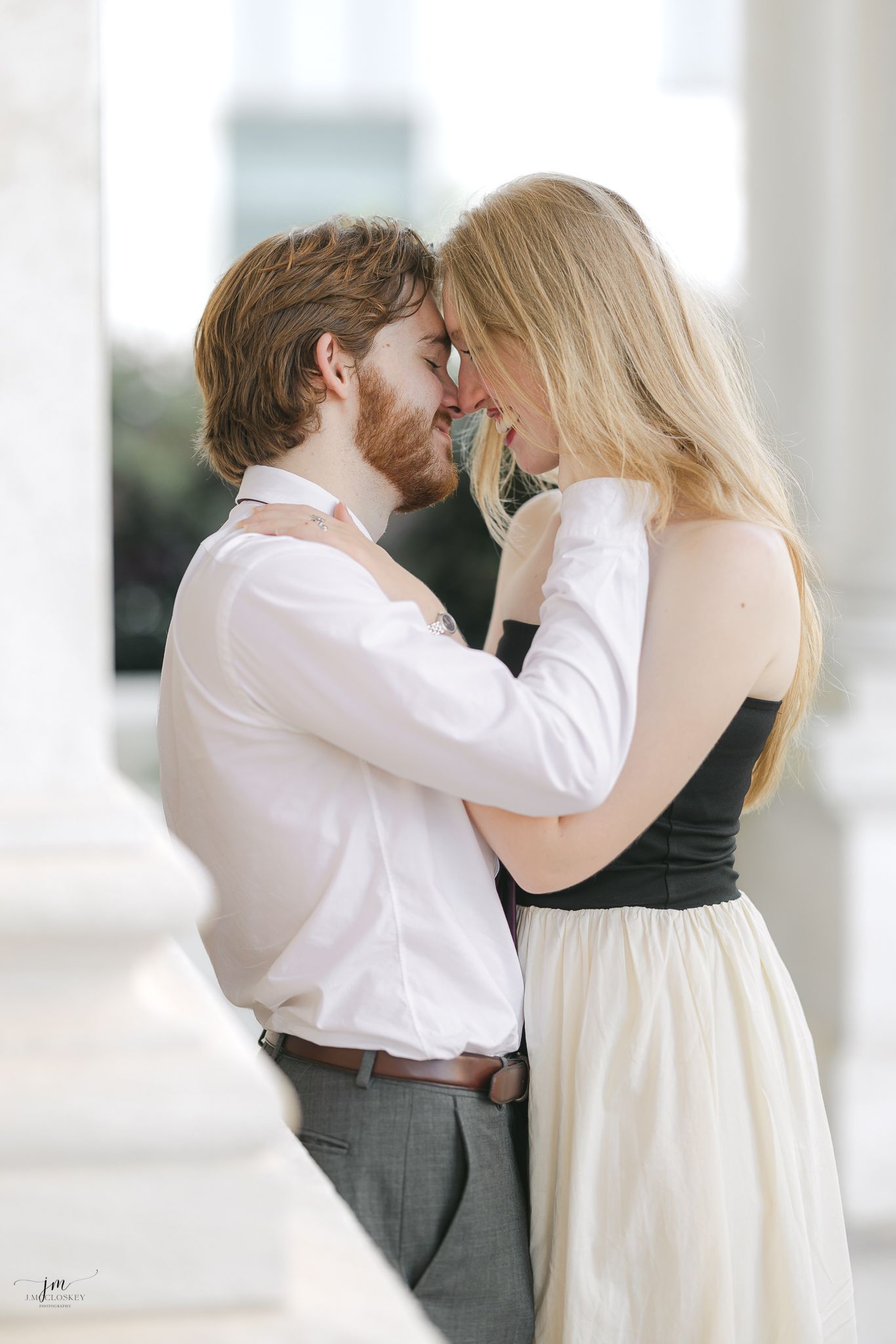 A tender moment between a couple in formal wear against white columns.