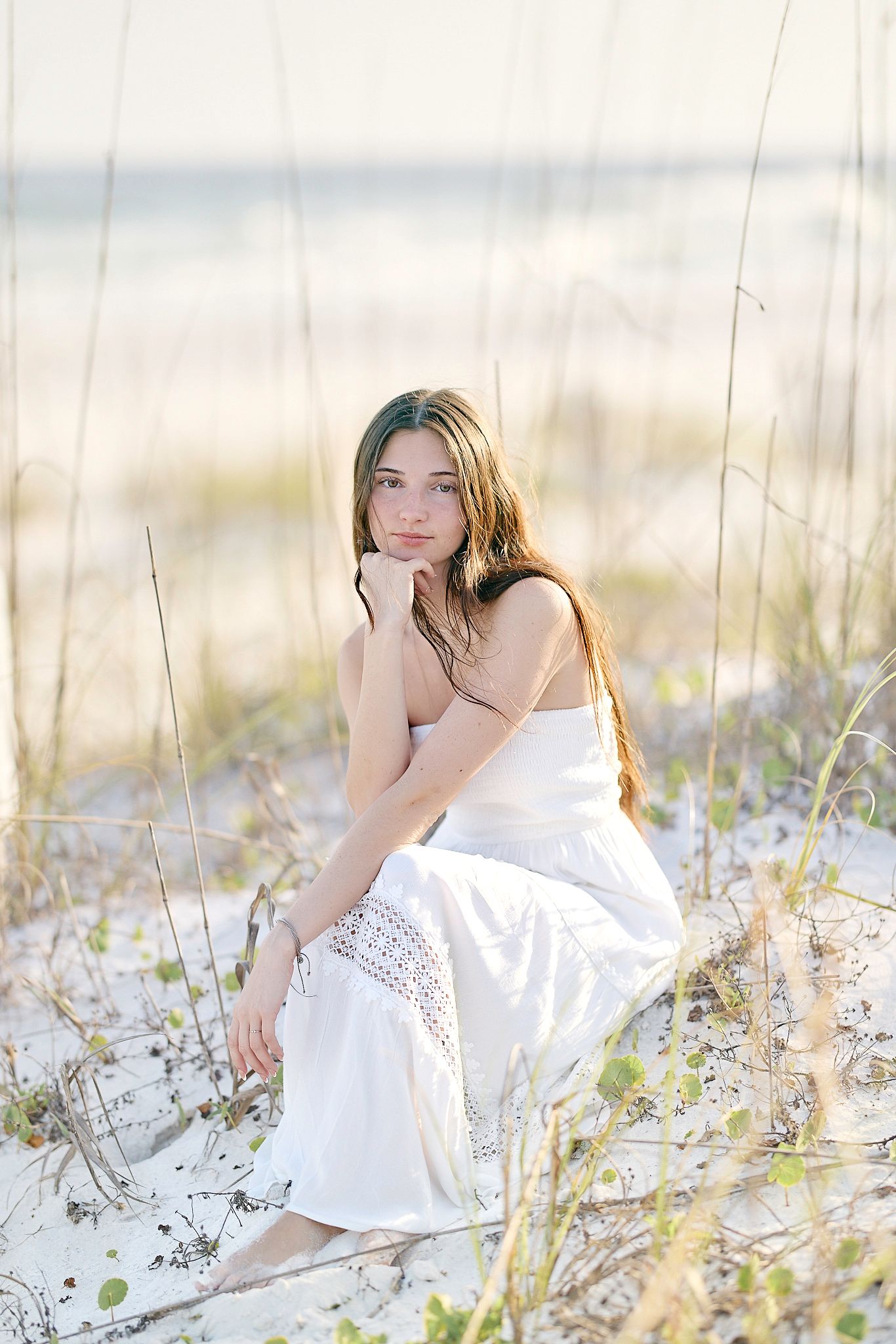 An ethereal beachside photo featuring a white sundress against coastal dunes and soft natural lighting.