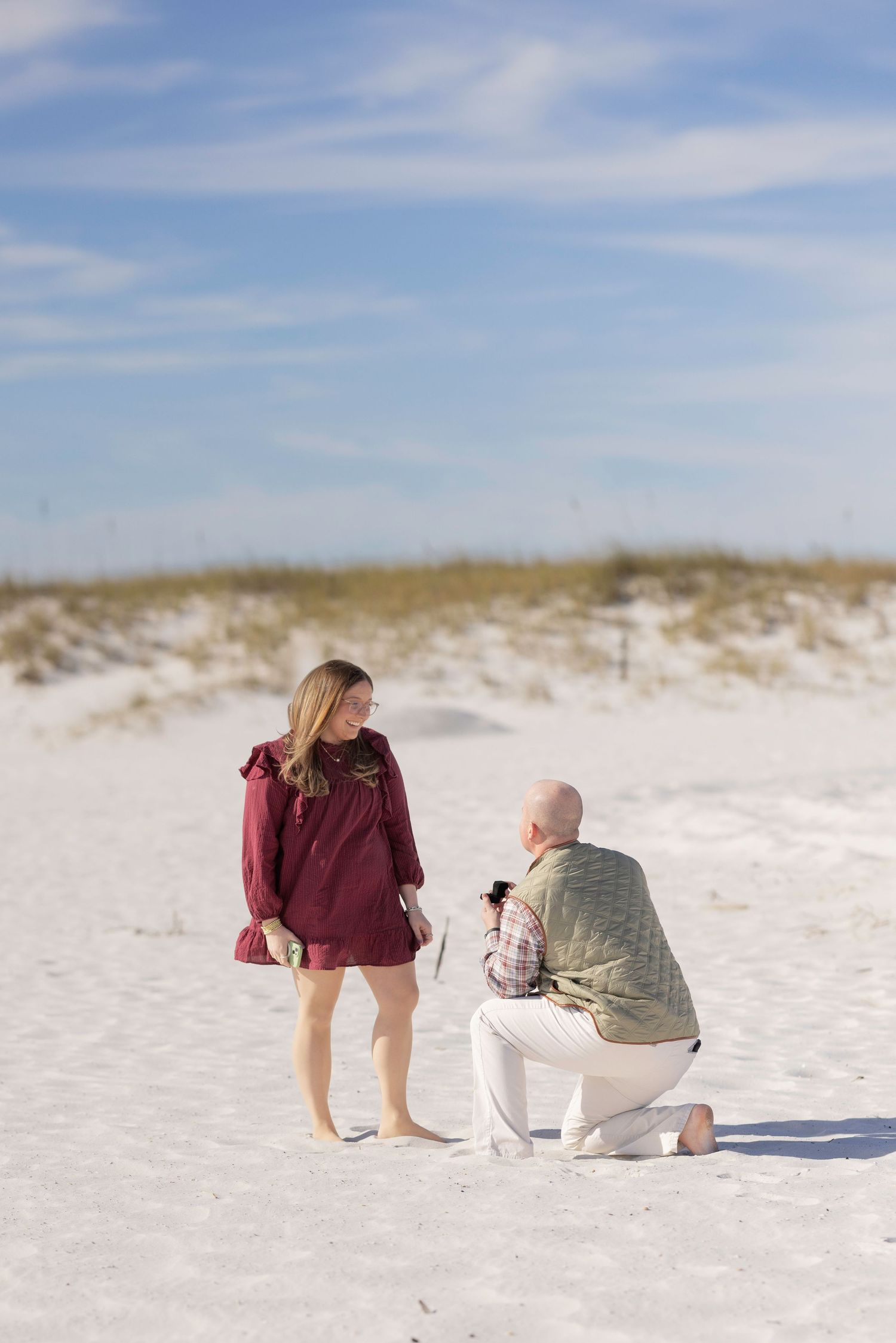 Two people share a tender moment on a pristine white sand beach under a bright blue sky.